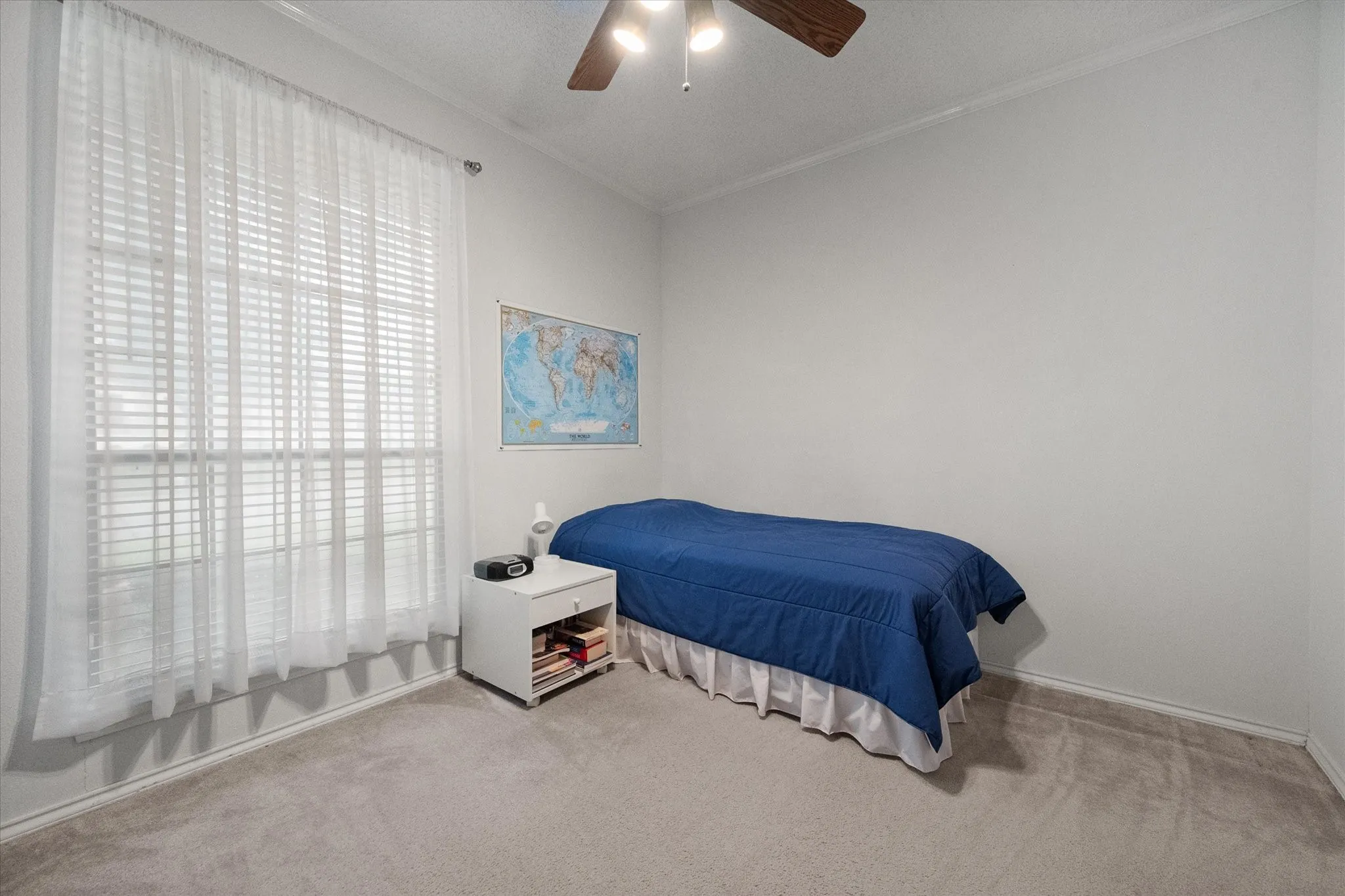 Carpeted room featuring a large window with blinds and sheer curtains, light-colored walls, and a ceiling fan with integrated lighting