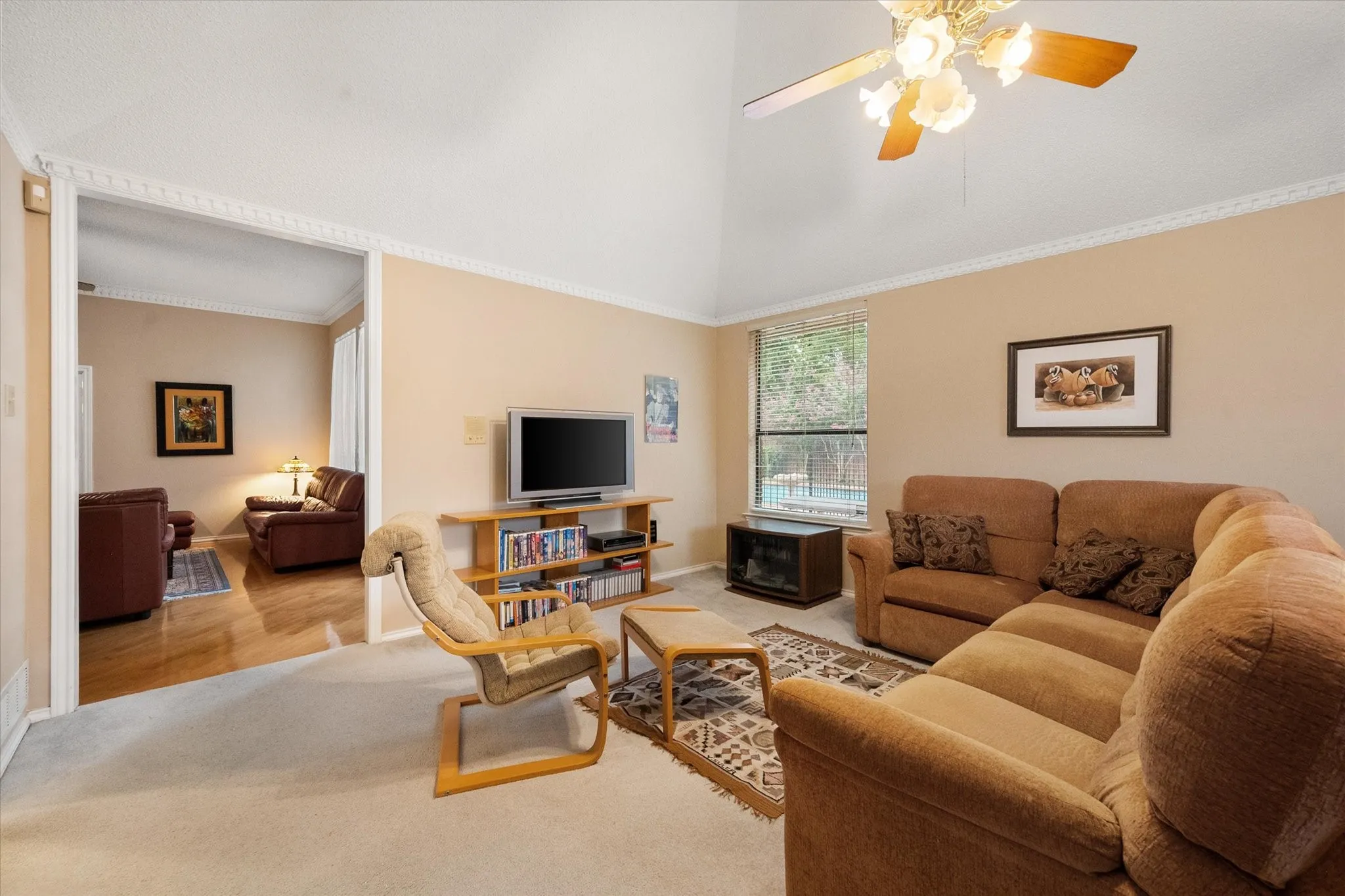 Living area with vaulted ceiling, crown molding, and a ceiling fan with integrated lighting