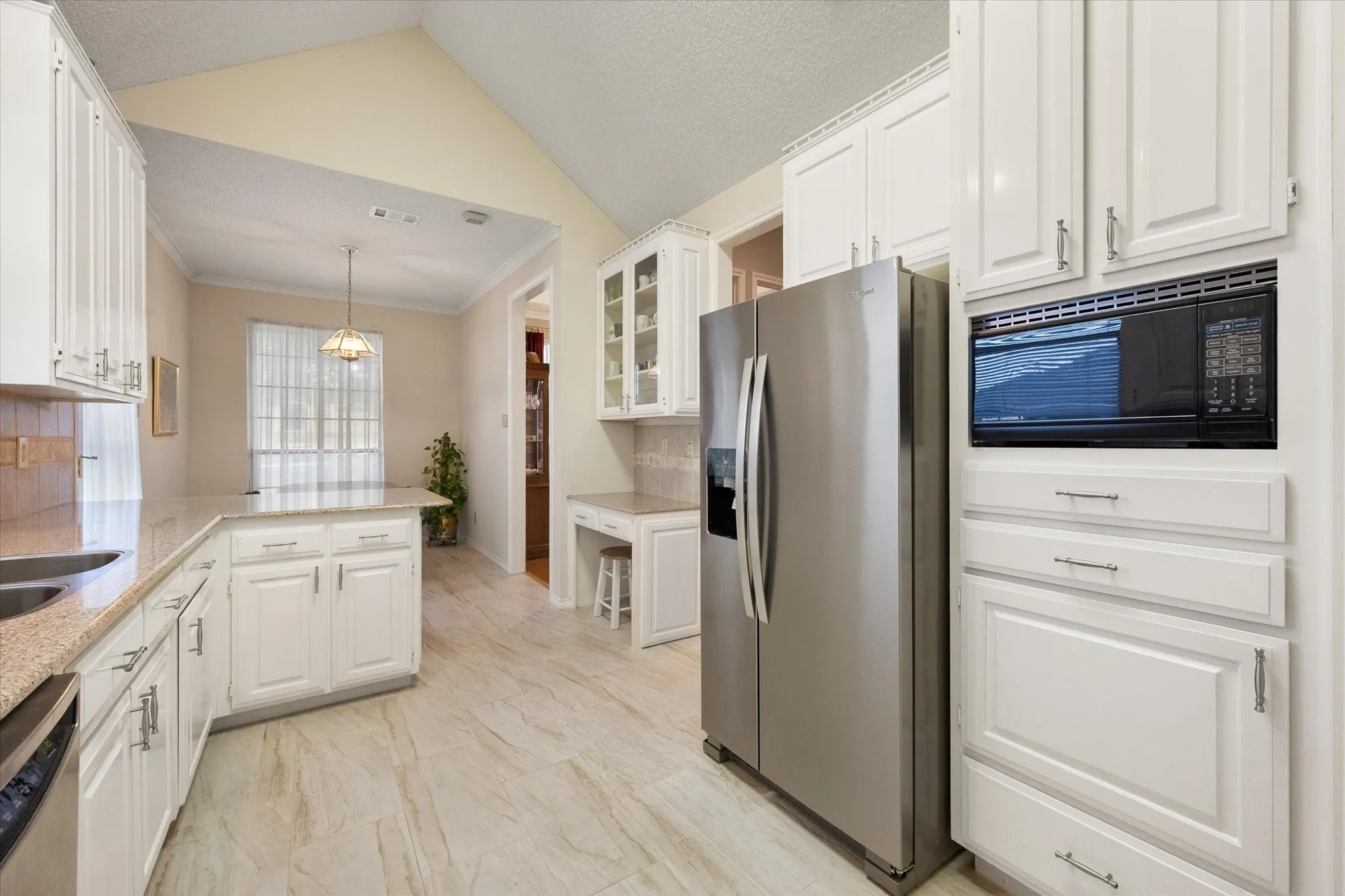 Kitchen featuring desk area, updated door pulls and plenty of storage, light-toned, Silestone countertops, tile flooring, and vaulted ceiling