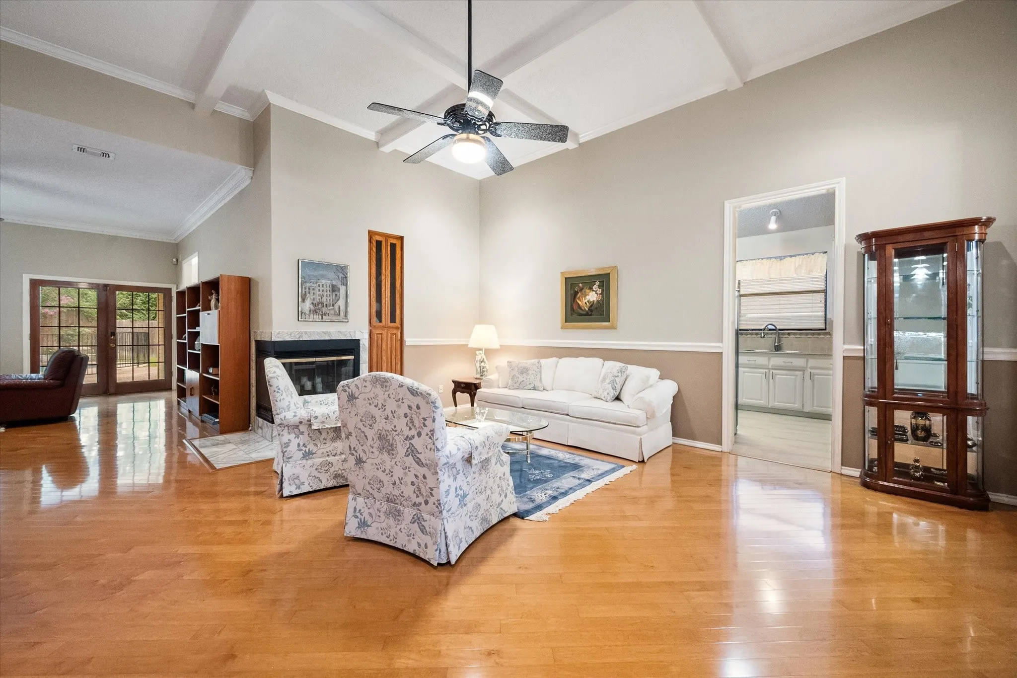 Spacious living area featuring high vaulted ceilings with exposed beams, light wood-finish flooring, a fireplace with a stone surround, and French doors