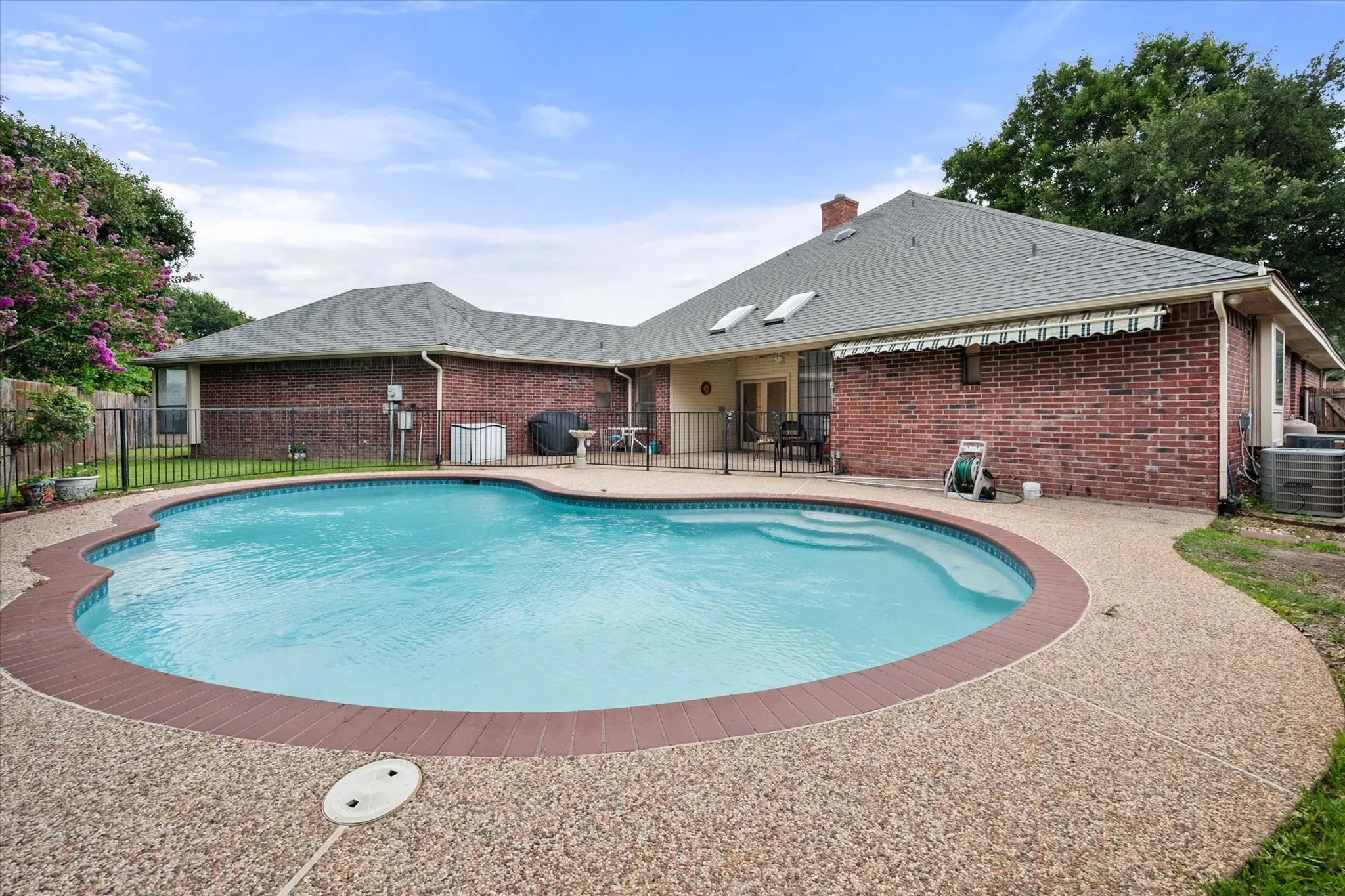 Oval-shaped swimming pool with an integrated spa, surrounded by an exposed aggregate concrete deck