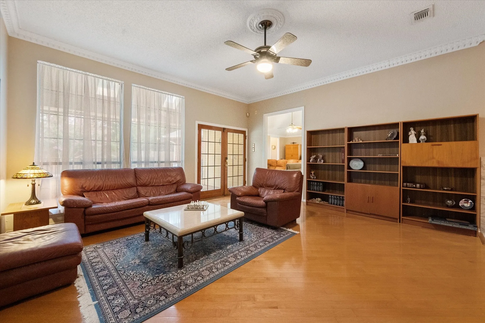 Spacious room featuring light wood-finish flooring, built-in shelving, two large windows, a ceiling fan with light fixture, and decorative crown molding