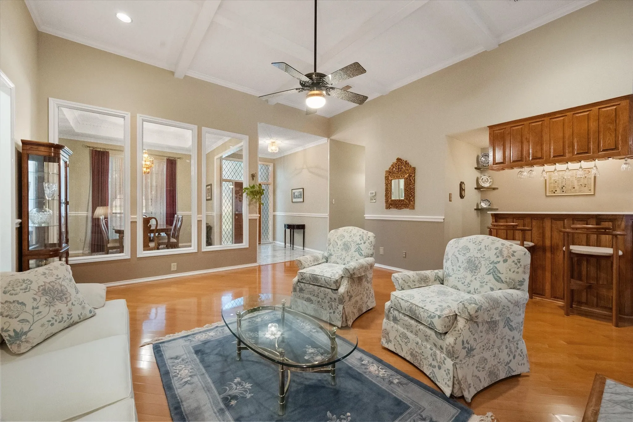 Spacious living area featuring high vaulted ceilings with exposed beams, wood-finish flooring, a built-in wet bar with upper cabinetry, and a ceiling fan with integrated lighting
