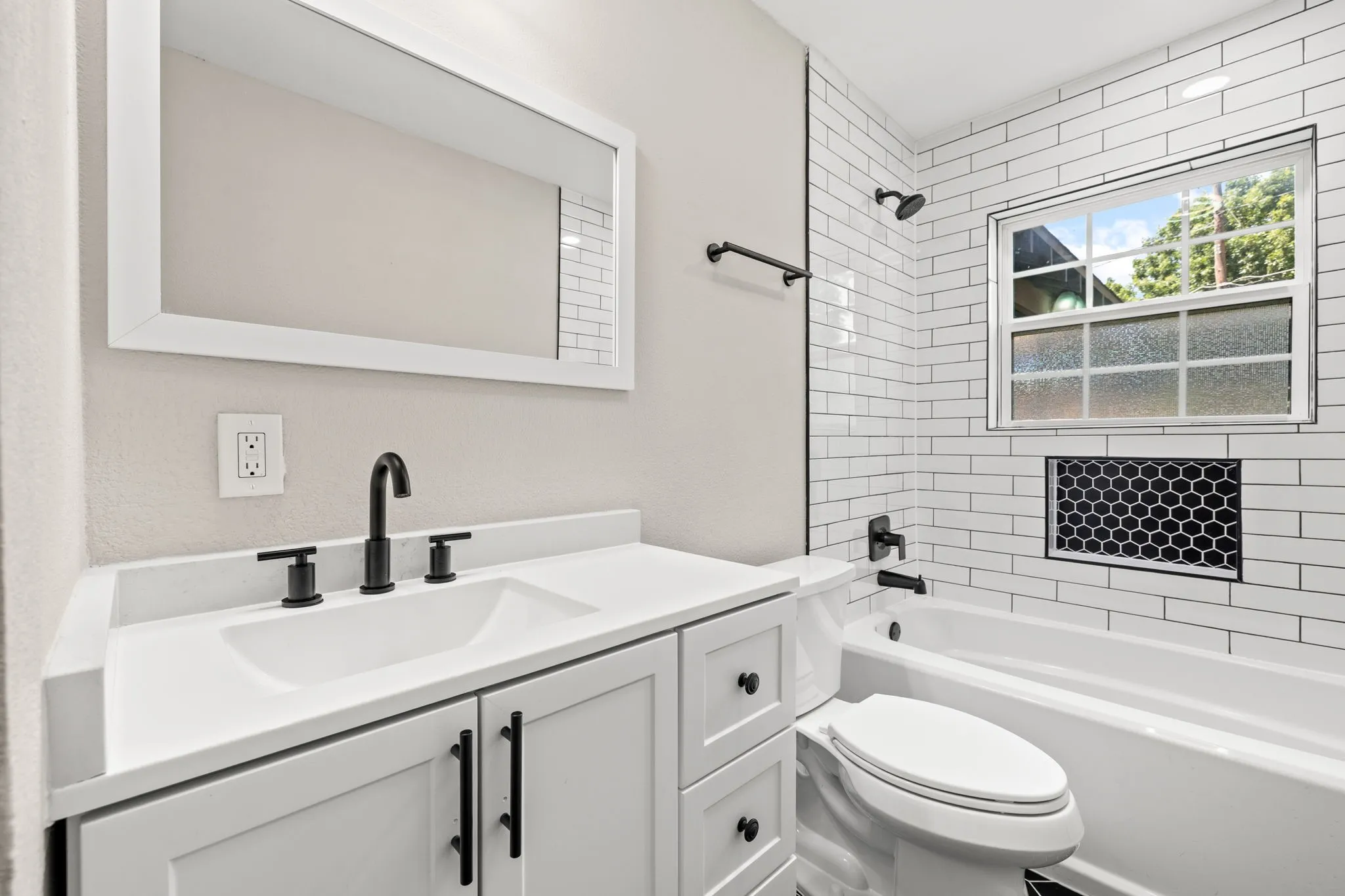White subway tile bath surround featuring a black hex tile niche and a window