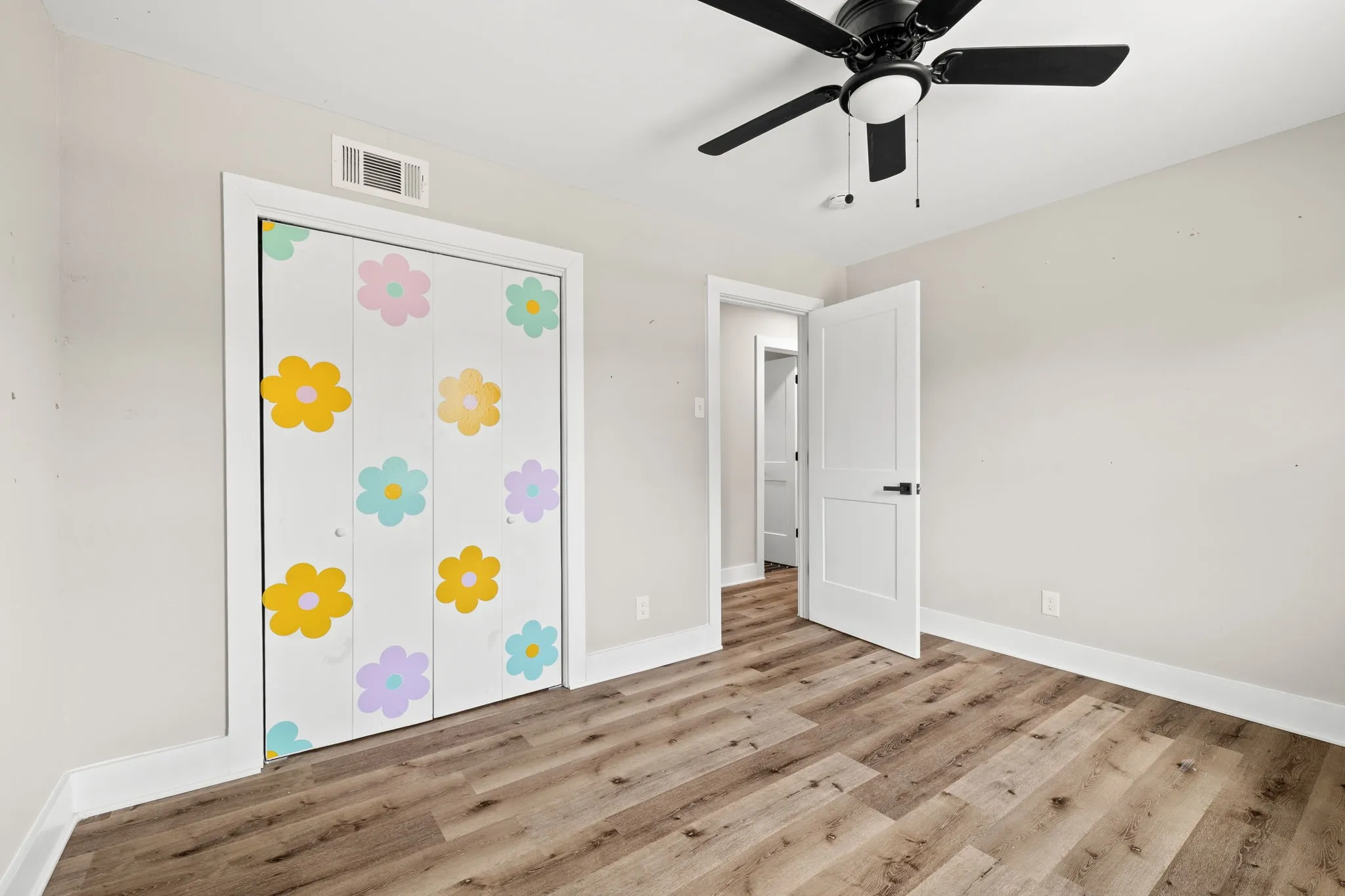 Room featuring wood-finish flooring, a contemporary black ceiling fan with integrated lighting, white baseboards, and a white interior door with black hardware