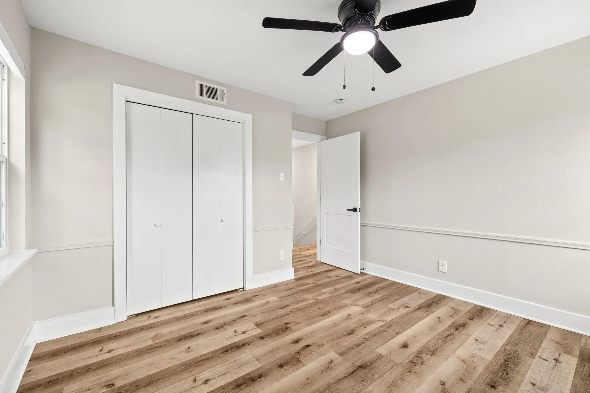 Room featuring wood-finish flooring, a ceiling fan with integrated lighting, and neutral-toned walls with wainscoting