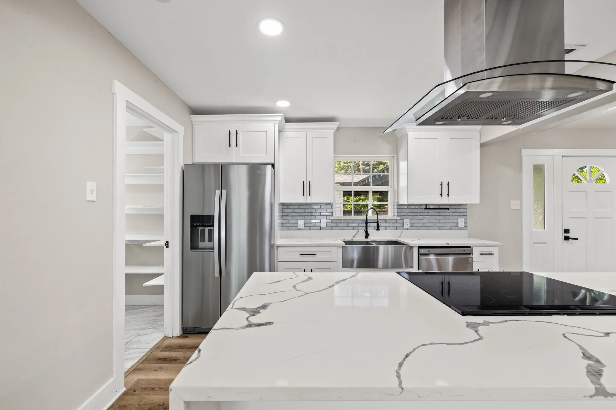 Modern kitchen featuring white shaker cabinetry, stainless steel appliances, a large island with an integrated cooktop, and a walk-in pantry