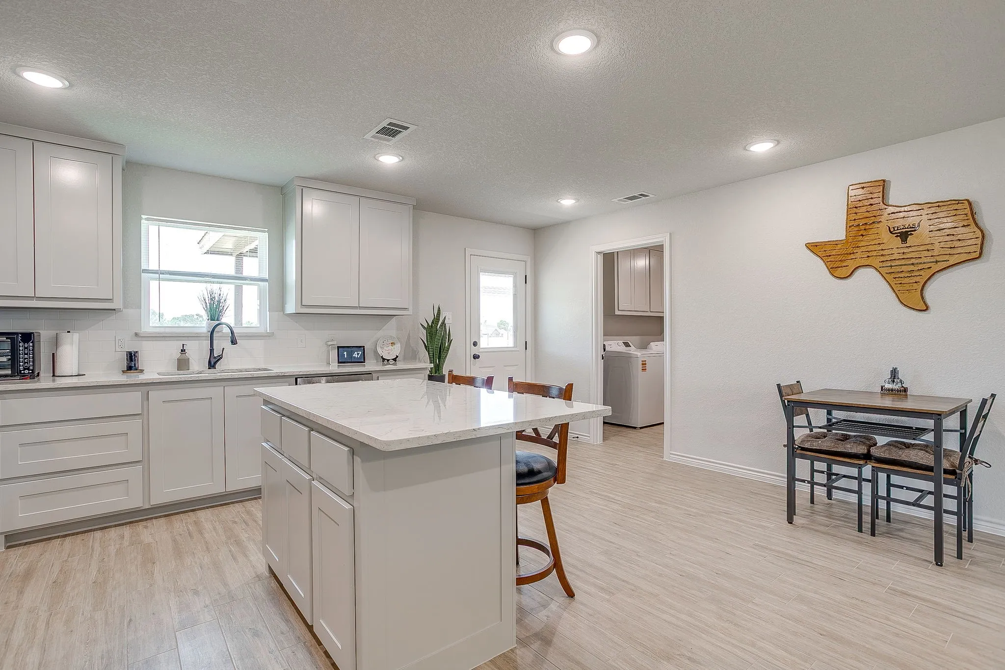 White shaker cabinetry, light wood-finish flooring, recessed lighting, white backsplash, and a central kitchen island with seating