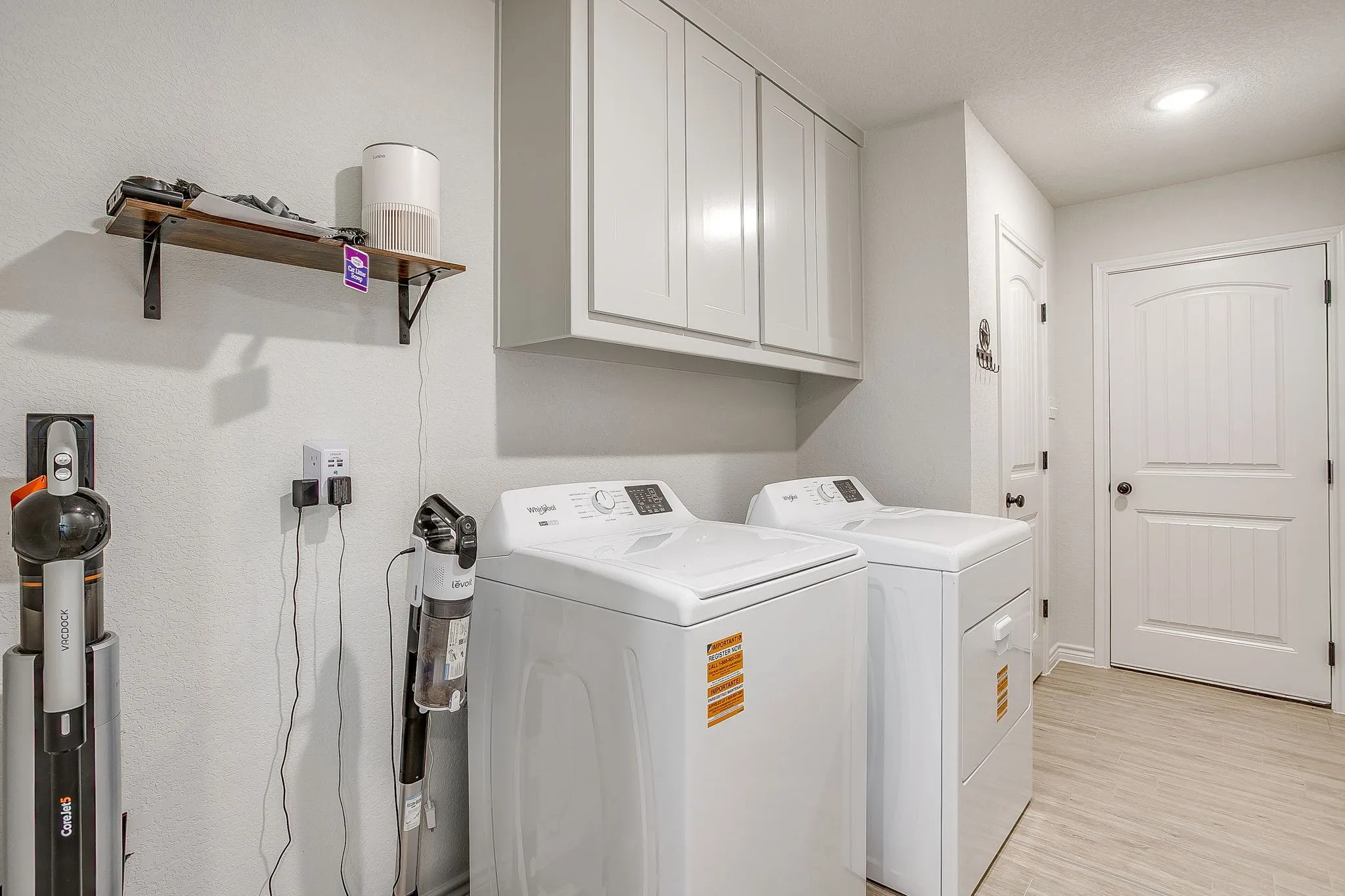 Laundry area with white cabinetry, wood-finish flooring, and arched panel doors