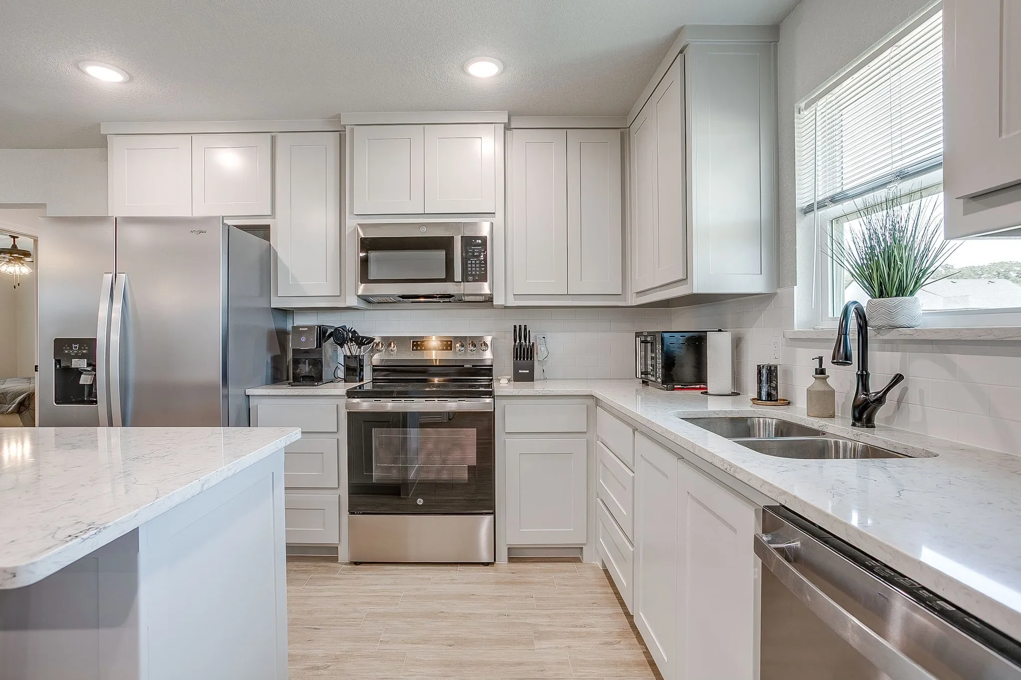 White shaker-style cabinetry with stainless steel appliances, light-toned wood-finish flooring, and light-toned countertops