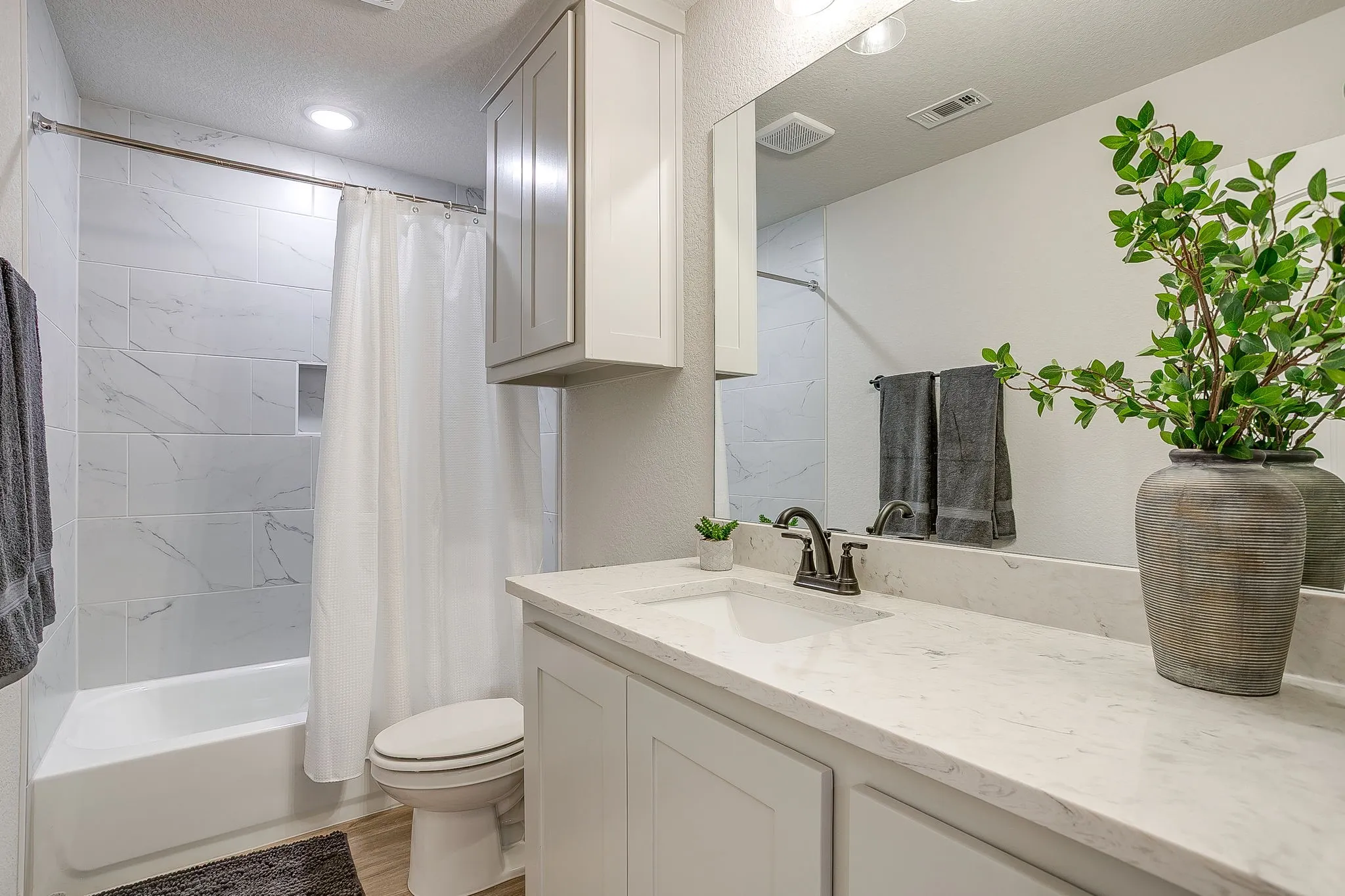 Contemporary bathroom featuring a white vanity with an integrated sink, a large wall-mounted mirror, and a bath/shower combination with white tile surround