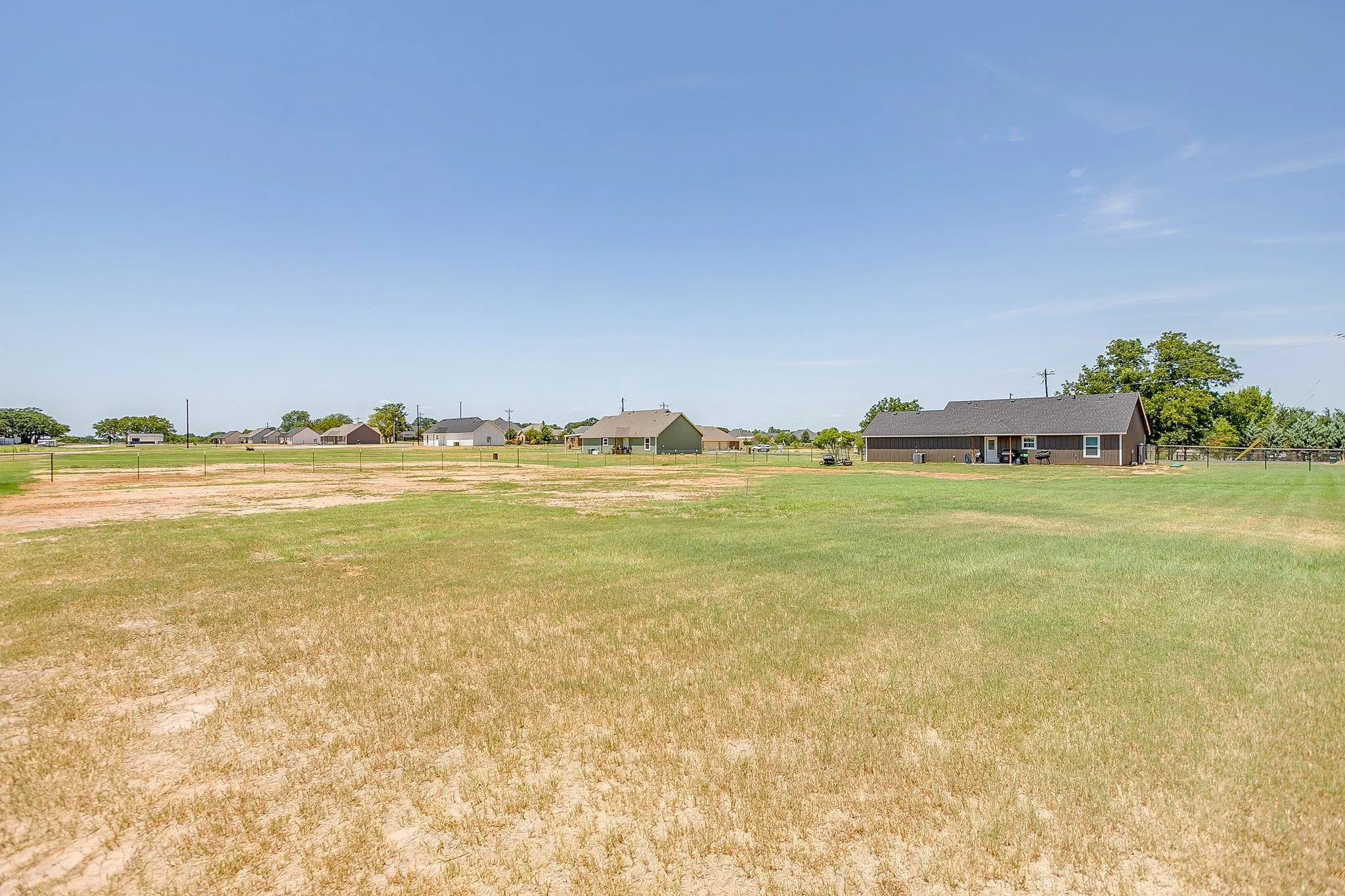 Expansive outdoor space featuring a large grassy area, a perimeter fence, and mature trees