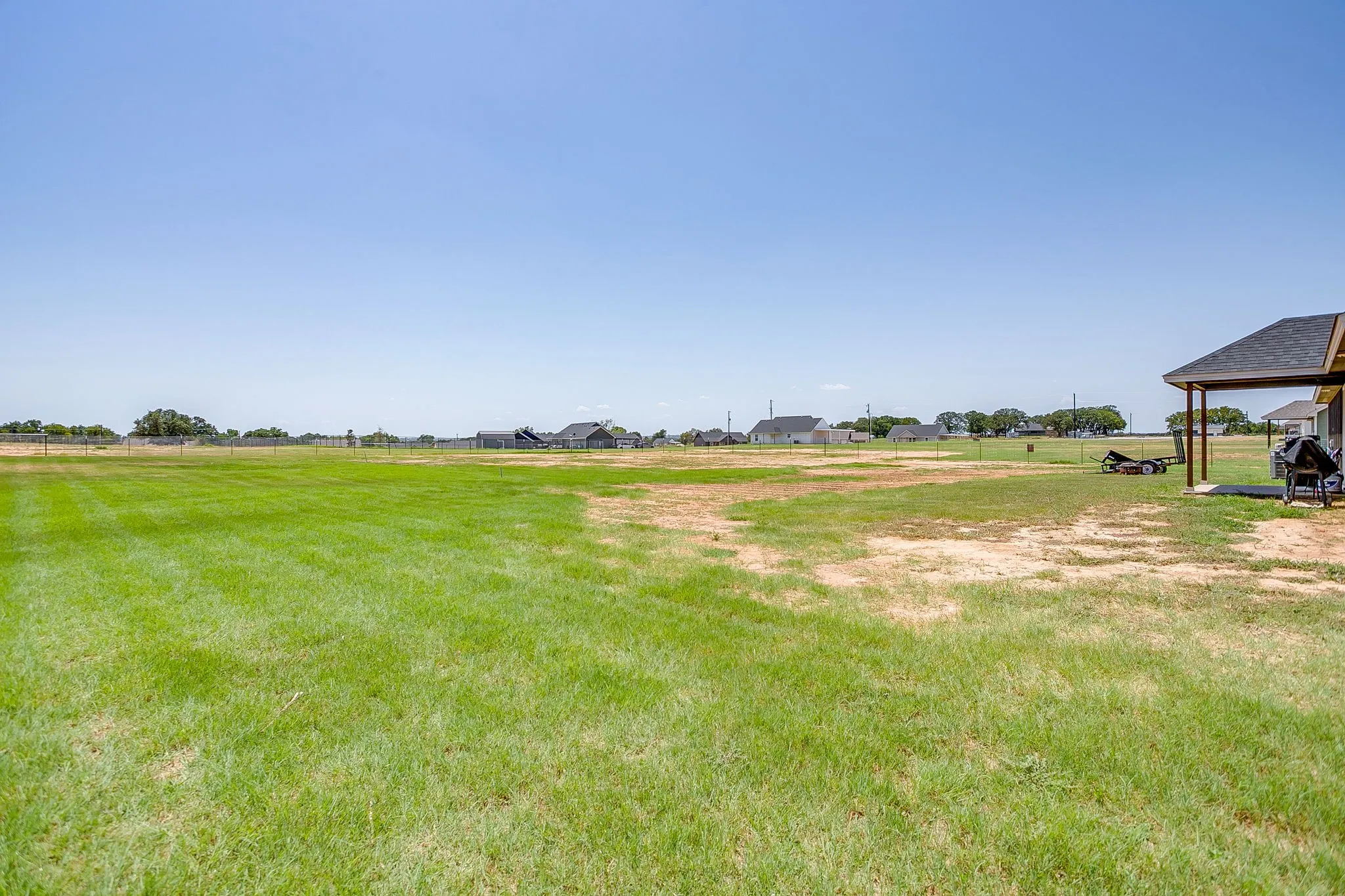 Expansive grass lawn with a covered patio featuring a dark shingle roof and structural support columns
