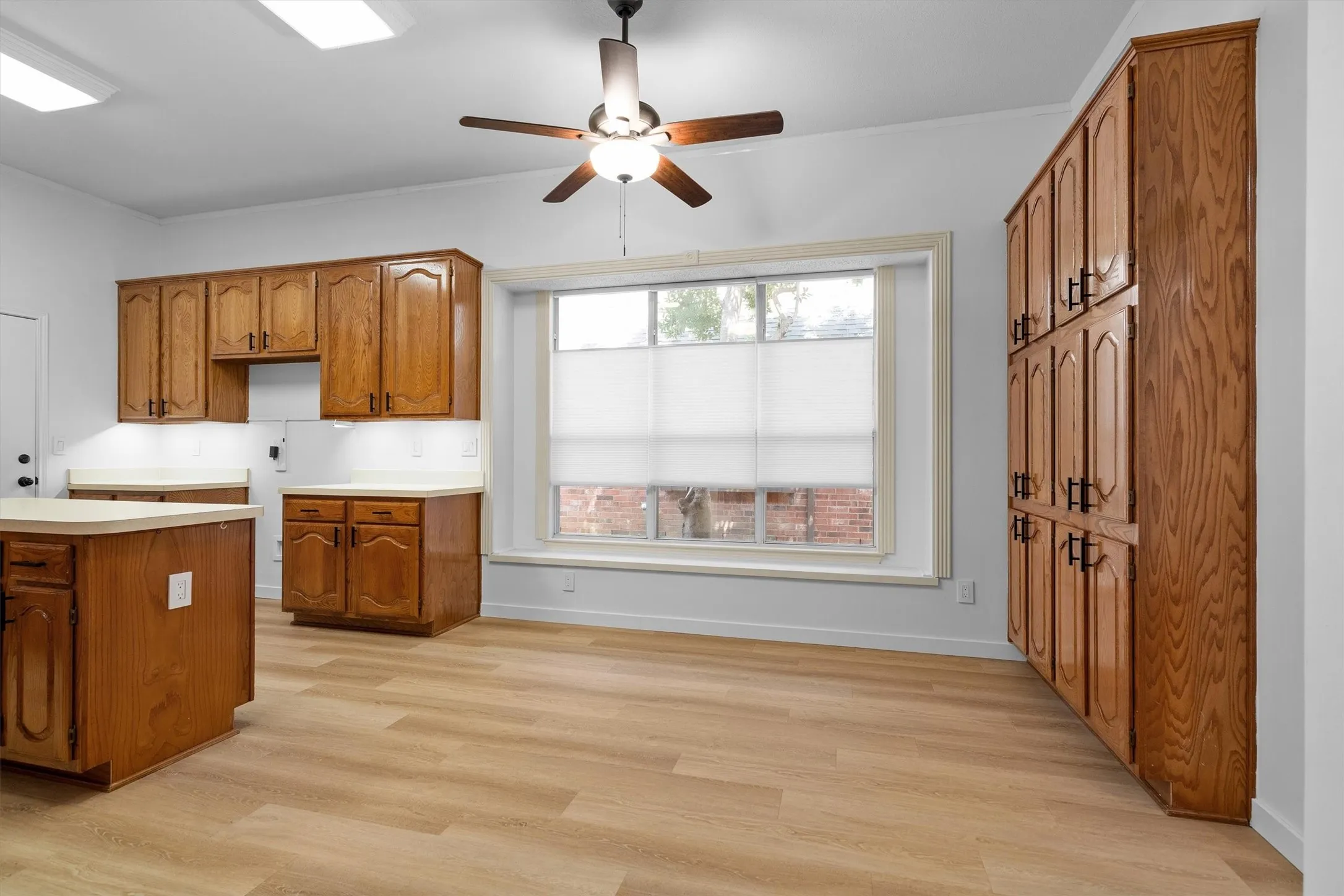 Spacious kitchen featuring extensive wood cabinetry, wood-finish flooring, a central island, and a window with a deep sill