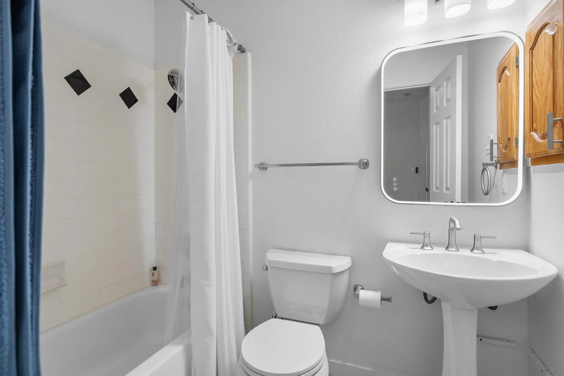 Full bathroom featuring a pedestal sink with a chrome faucet, a toilet, and a shower-over-tub with white subway tile and black accent tiles