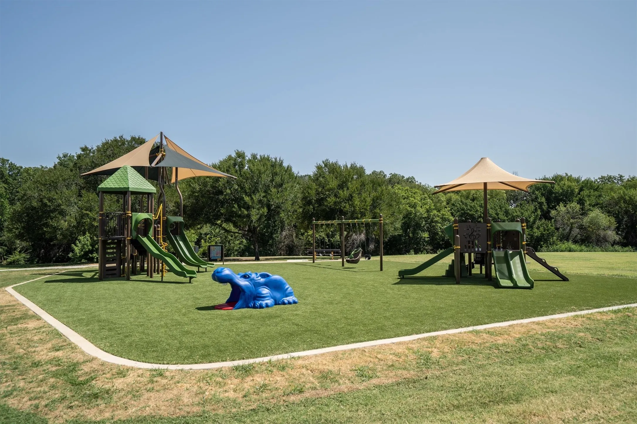 Recreational area featuring two play structures with slides, a swing set, and a blue animal-shaped climbing feature, all situated on artificial turf