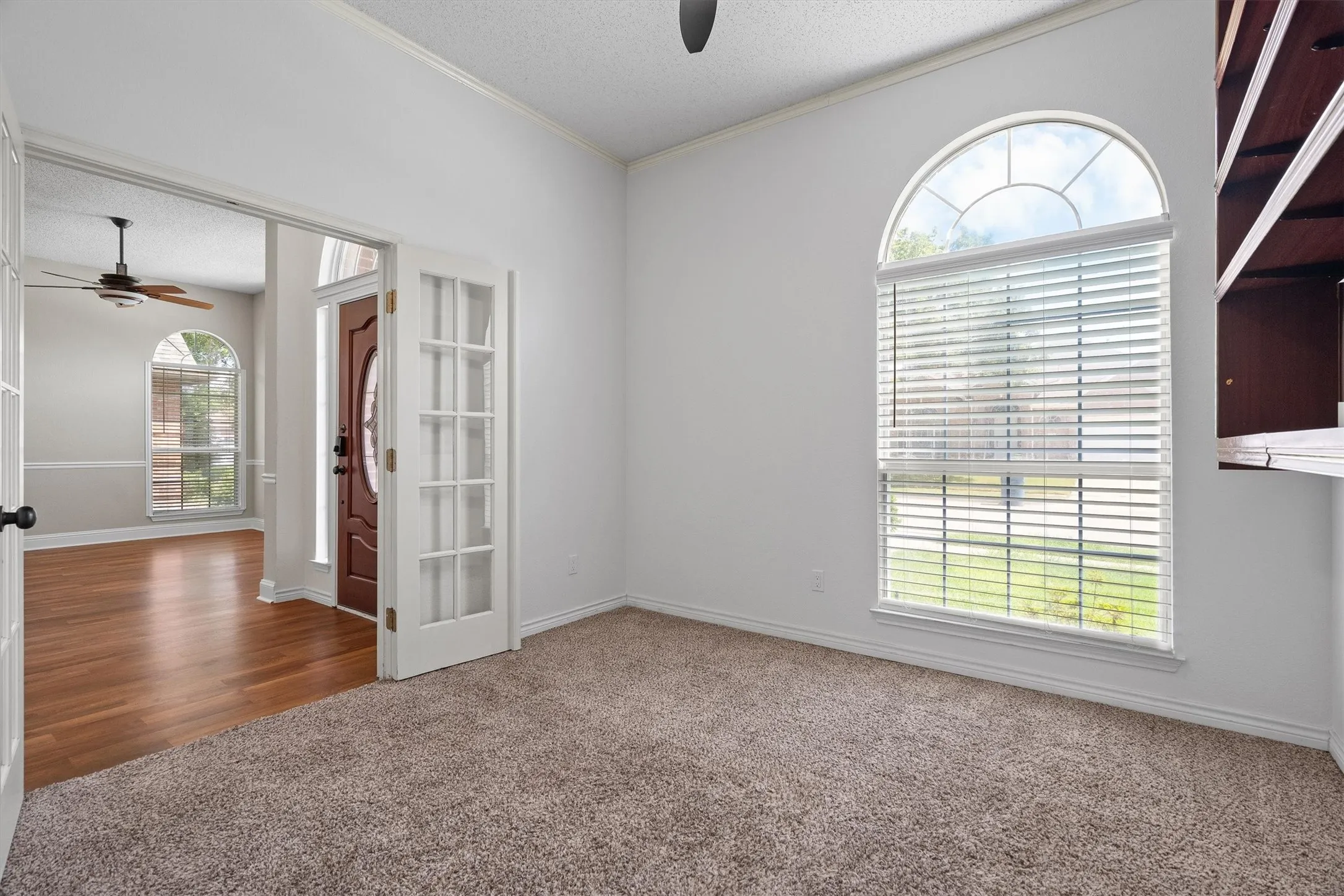 Carpeted room featuring an arched window with blinds, French doors, and crown molding