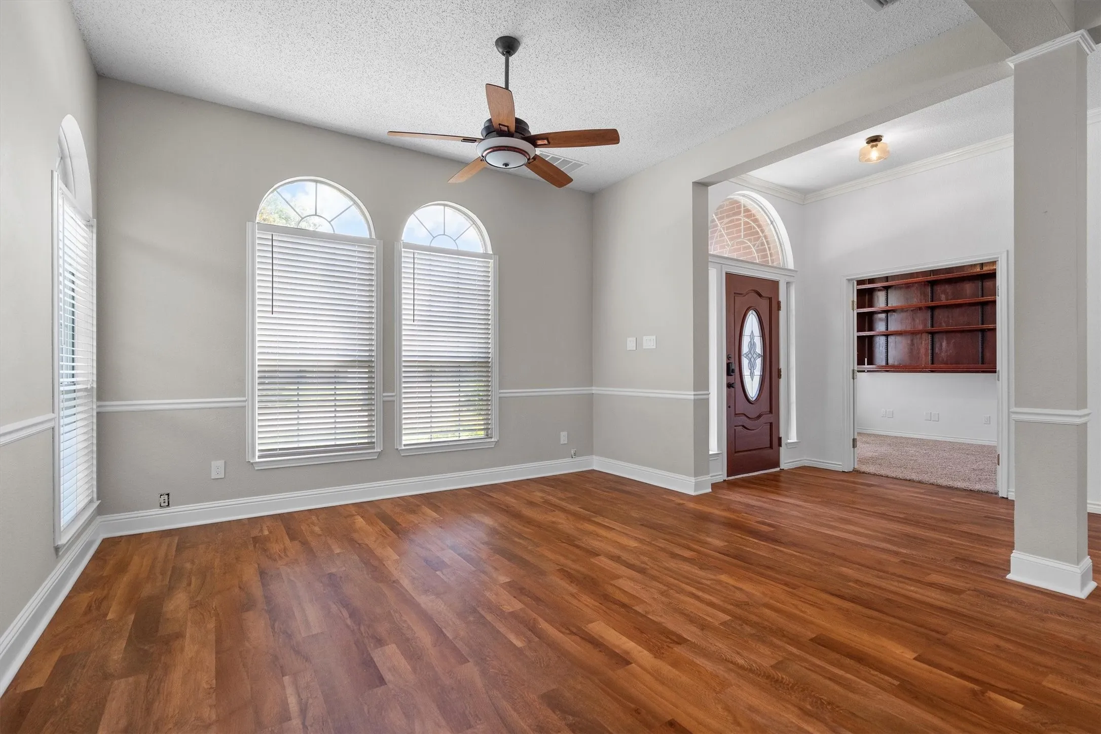Spacious room featuring wood-finish flooring, a ceiling fan, and multiple arched windows with blinds