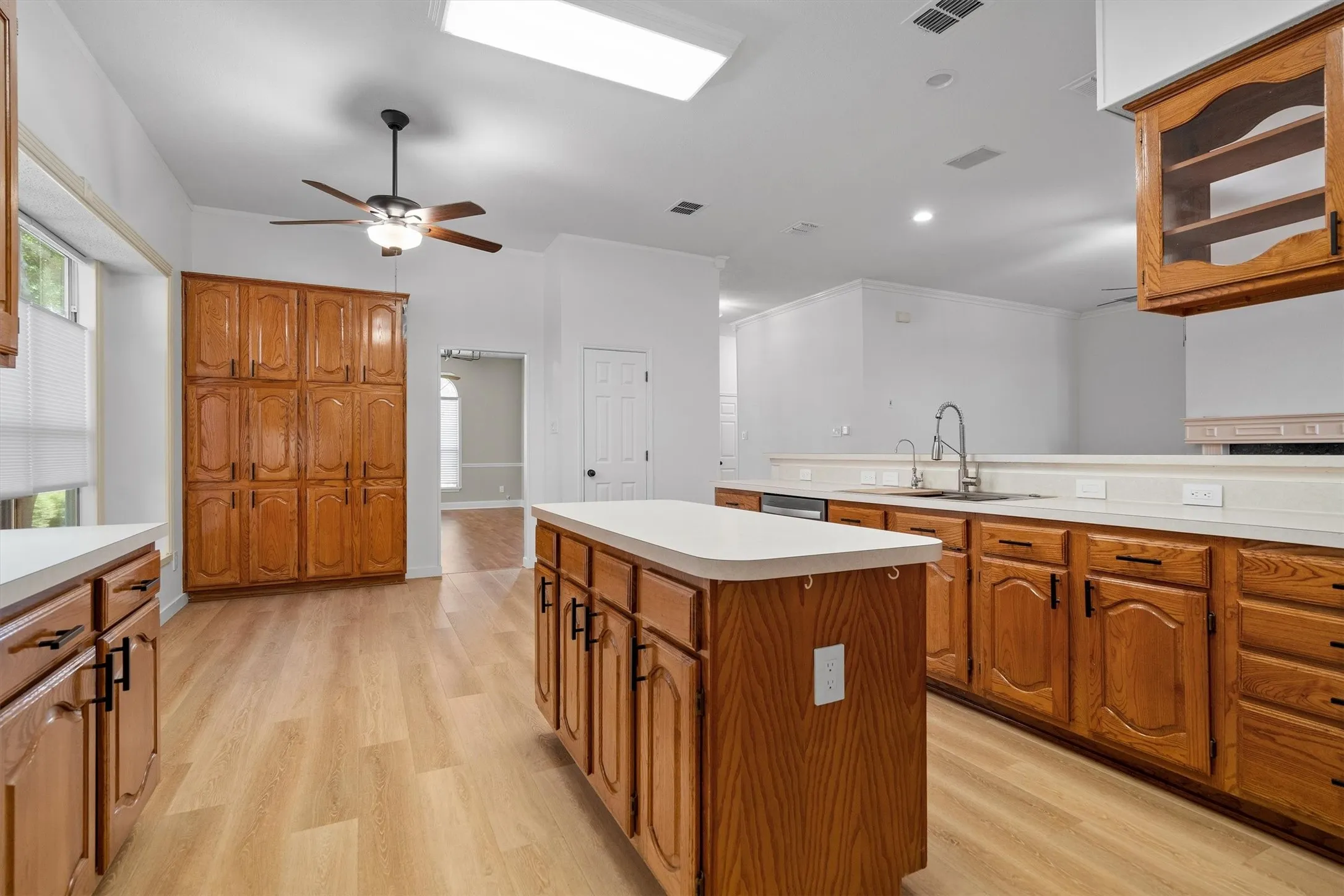 Bright kitchen featuring a central island, wood-finish flooring, abundant cabinetry, a built-in dishwasher, and a double basin sink