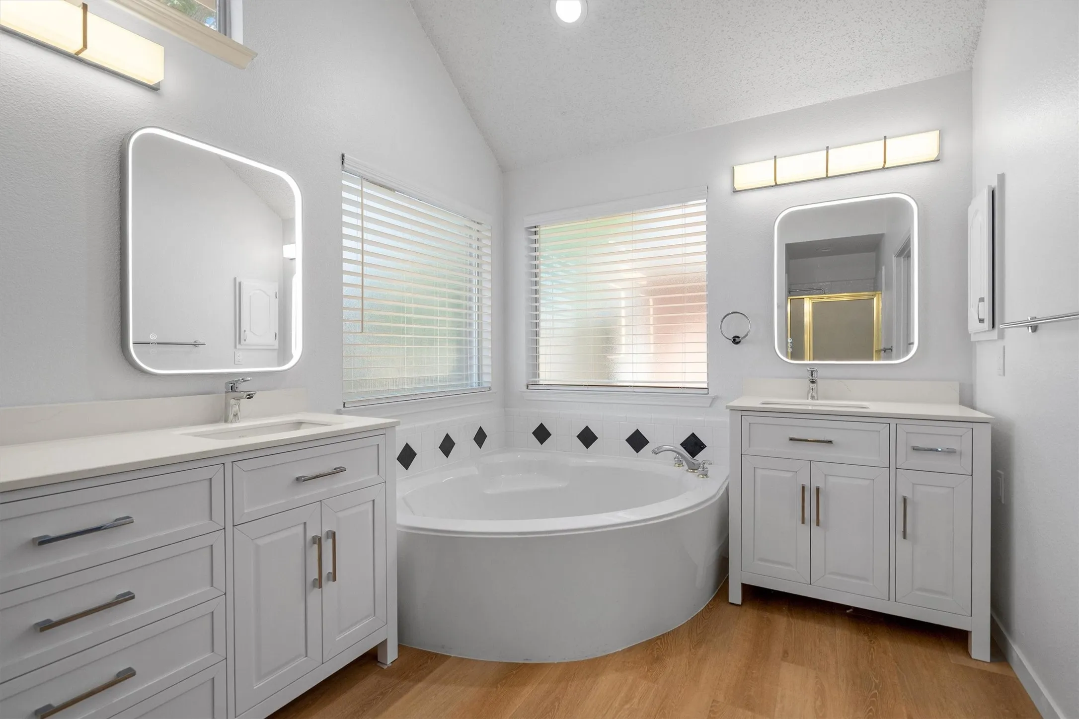 Spacious bathroom featuring a built-in corner soaking tub, dual vanity cabinets with undermount sinks, and contemporary illuminated mirrors