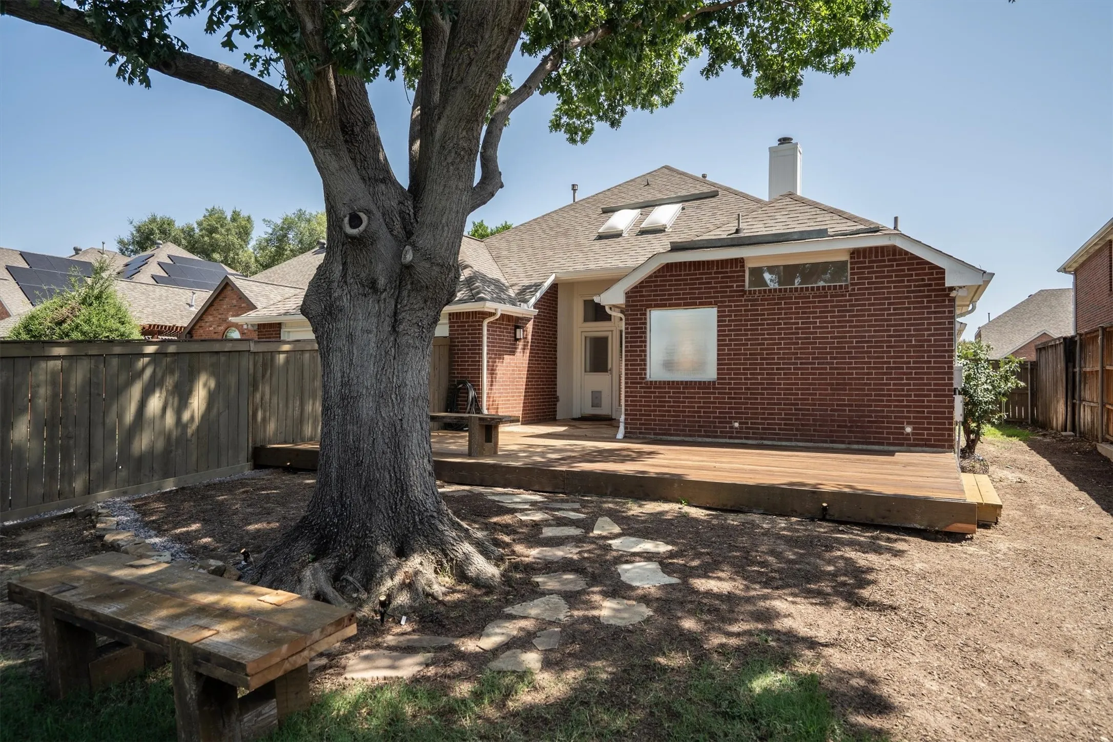 Expansive backyard featuring a large tree providing ample shade, a wood privacy fence, and a spacious wood deck