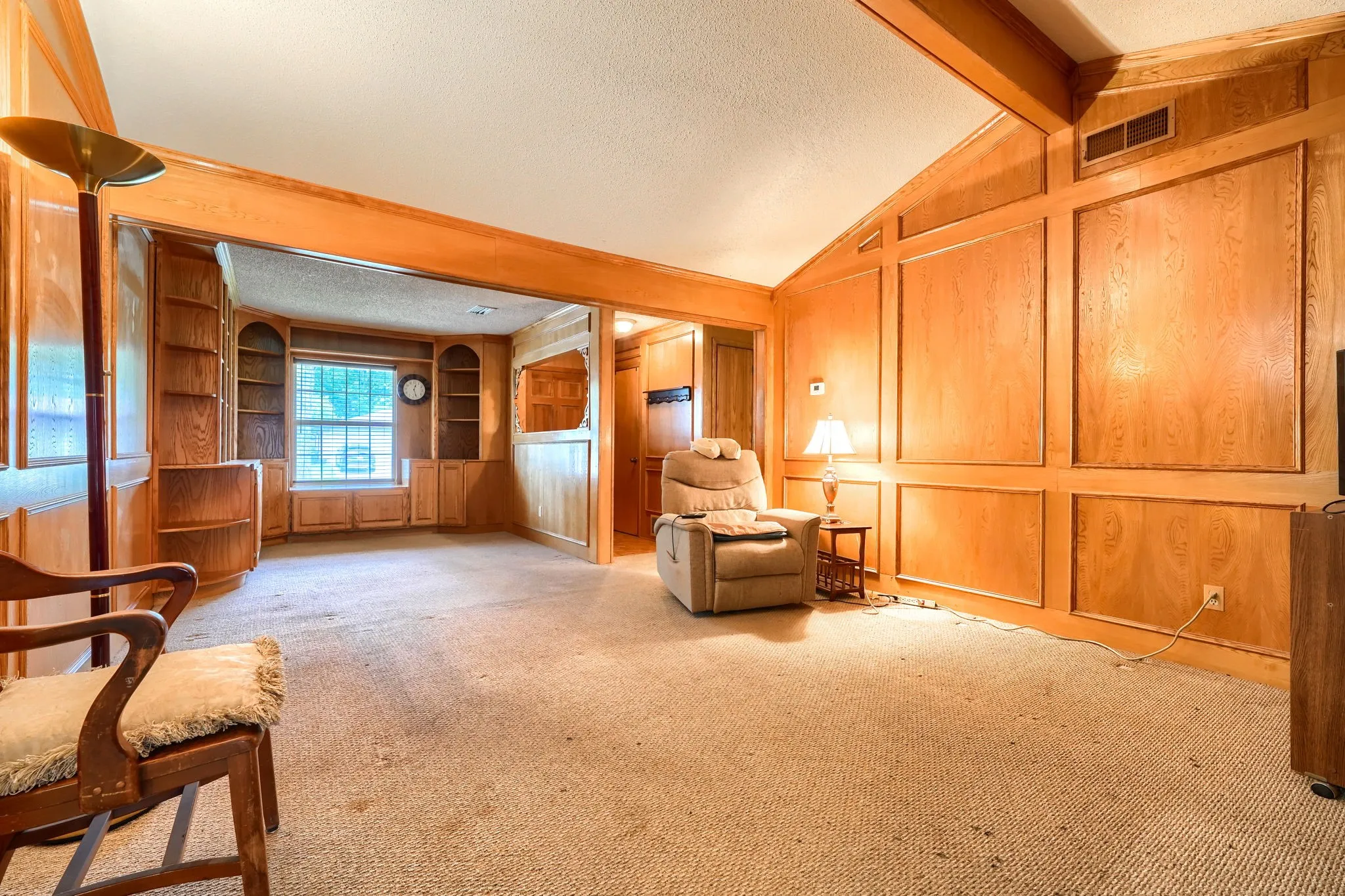 Carpeted room featuring extensive wood paneling, an arched entryway, and a vaulted ceiling