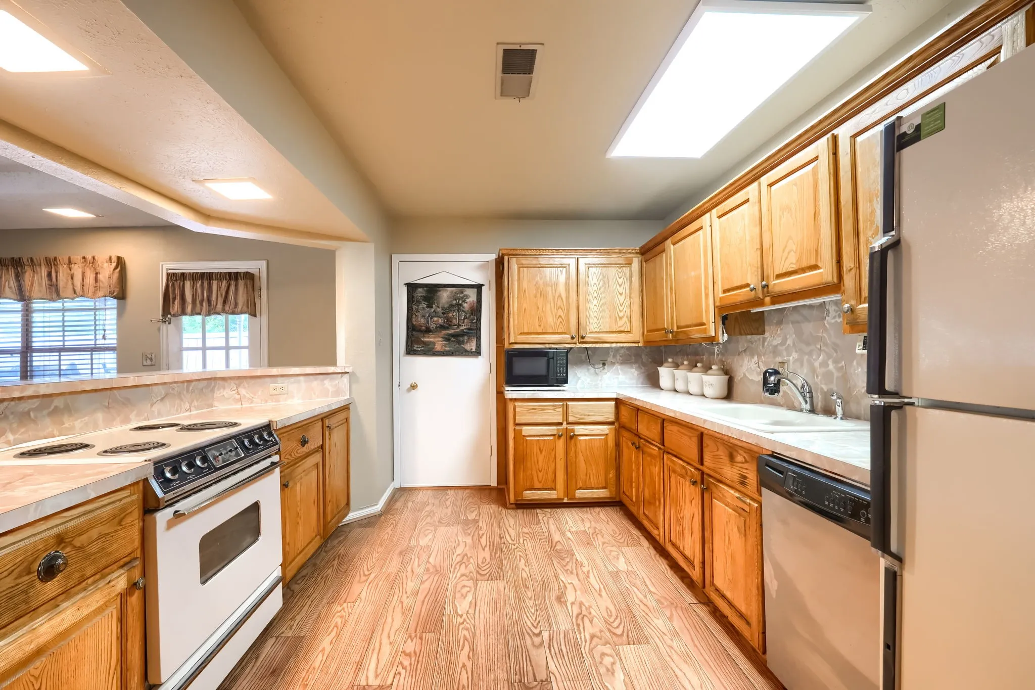 Kitchen featuring wood-finish flooring, oak cabinetry, a built-in electric range, and a breakfast bar opening