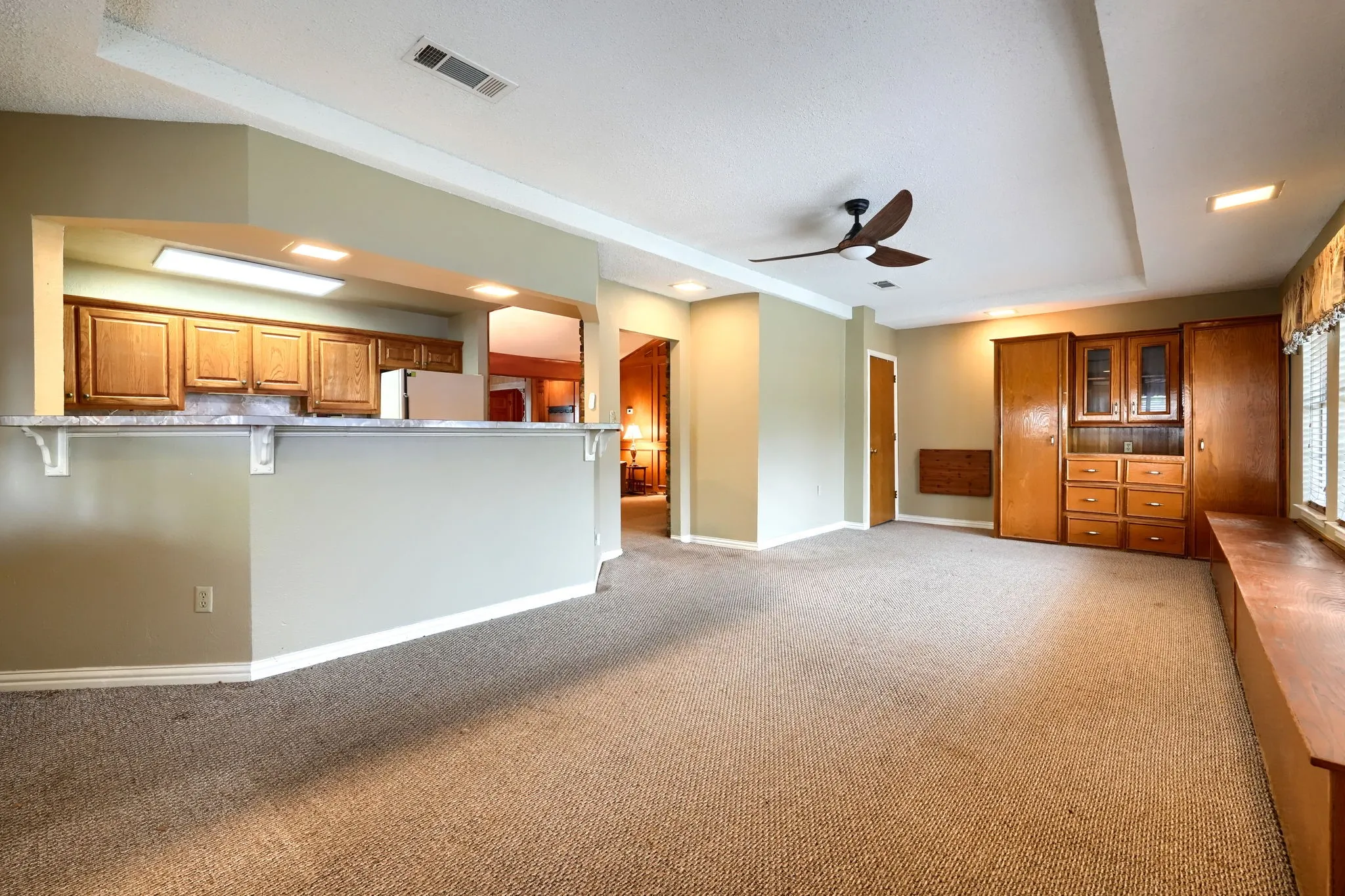 Expansive living area featuring a breakfast bar with a stone-finish countertop, a built-in entertainment center with glass-front cabinetry, a window bench with storage, a ceiling fan, and recessed lighting