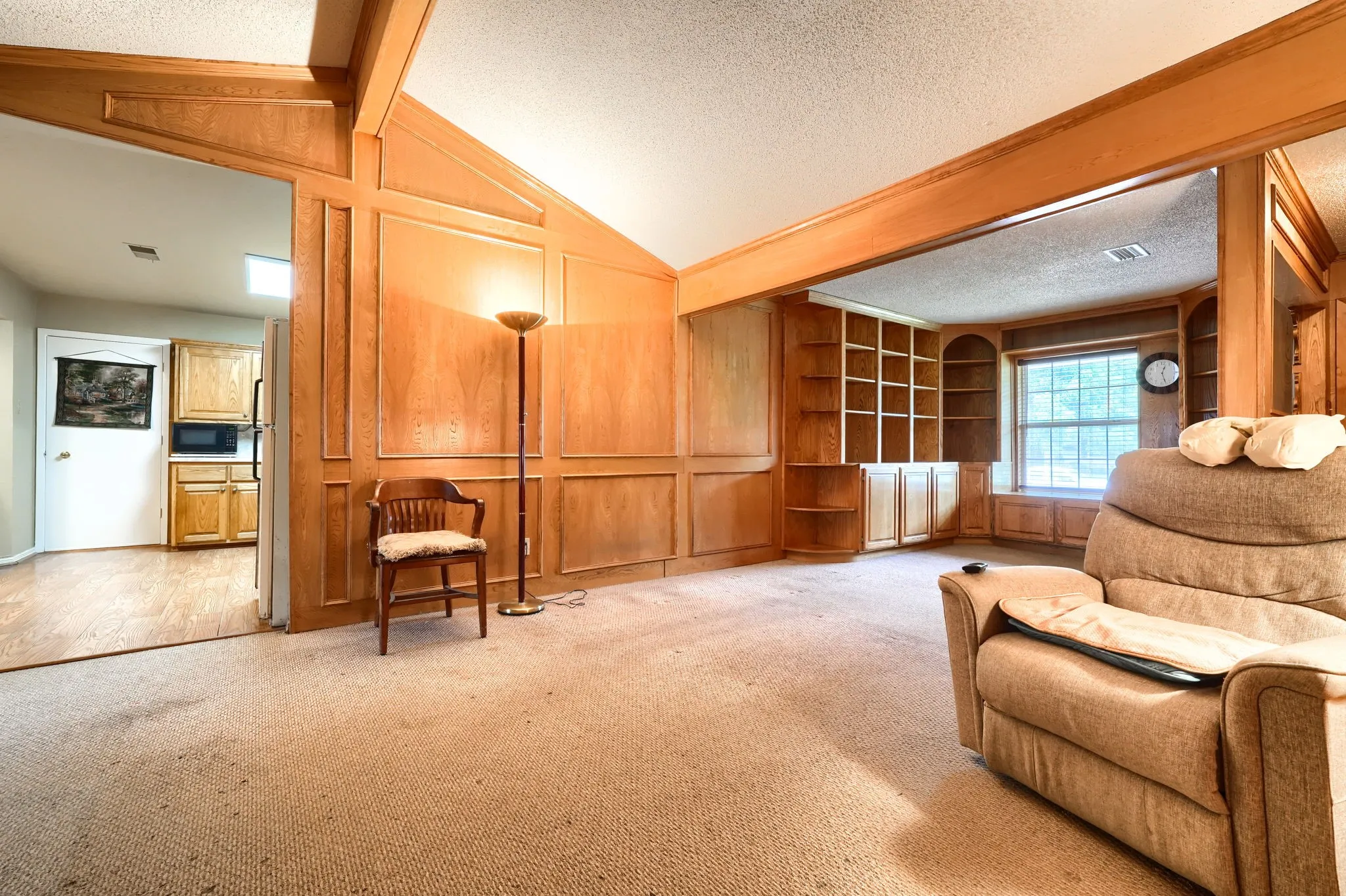 Spacious room featuring wood paneling, exposed wood beams, built-in shelving, a large window, and carpet flooring
