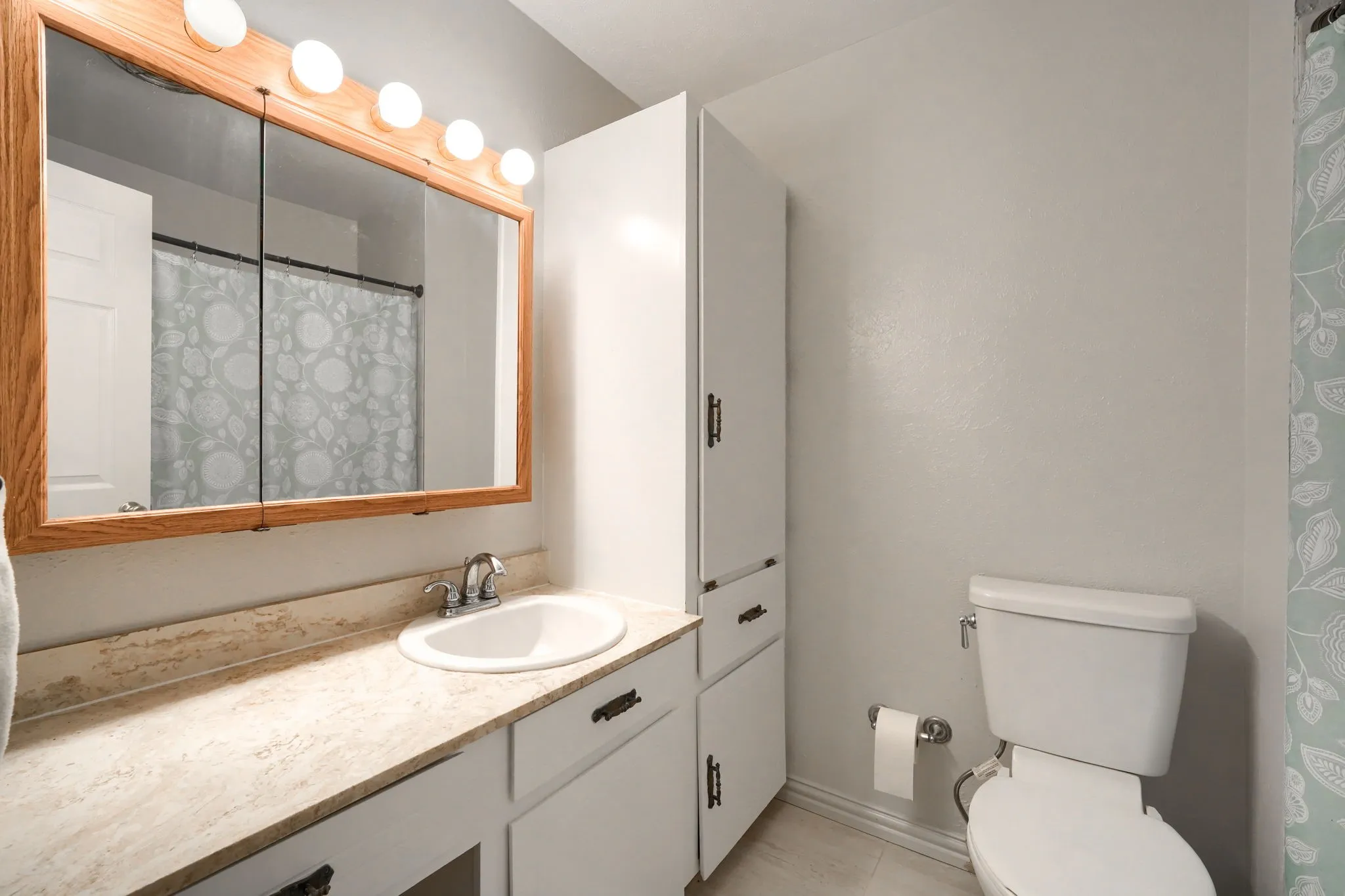 Bathroom featuring an integrated sink, textured countertop, and white cabinetry with dark hardware