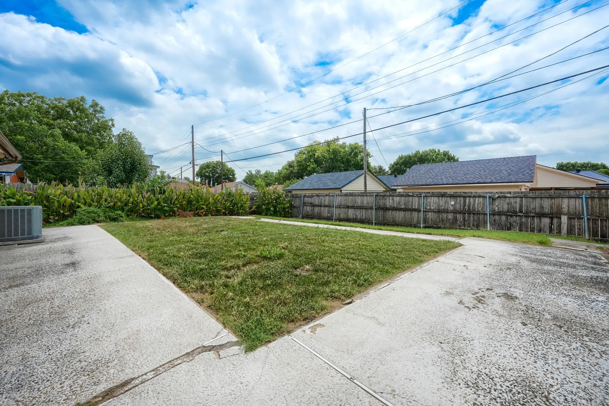 Expansive backyard with a large concrete patio, a sizable lawn area, mature perimeter landscaping, and a wood privacy fence