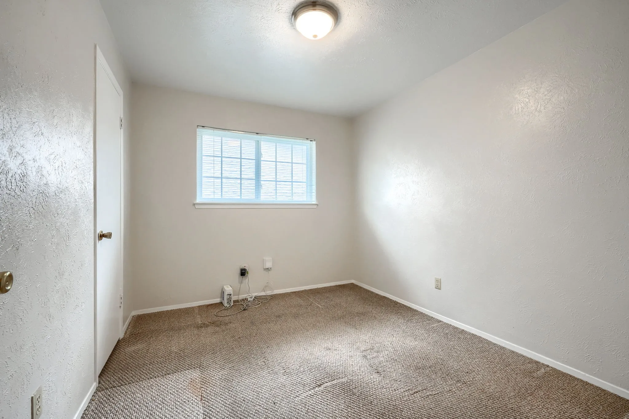 Neutral tone wall paint with textured finish, carpet flooring, a single window, and a flush mount ceiling light fixture