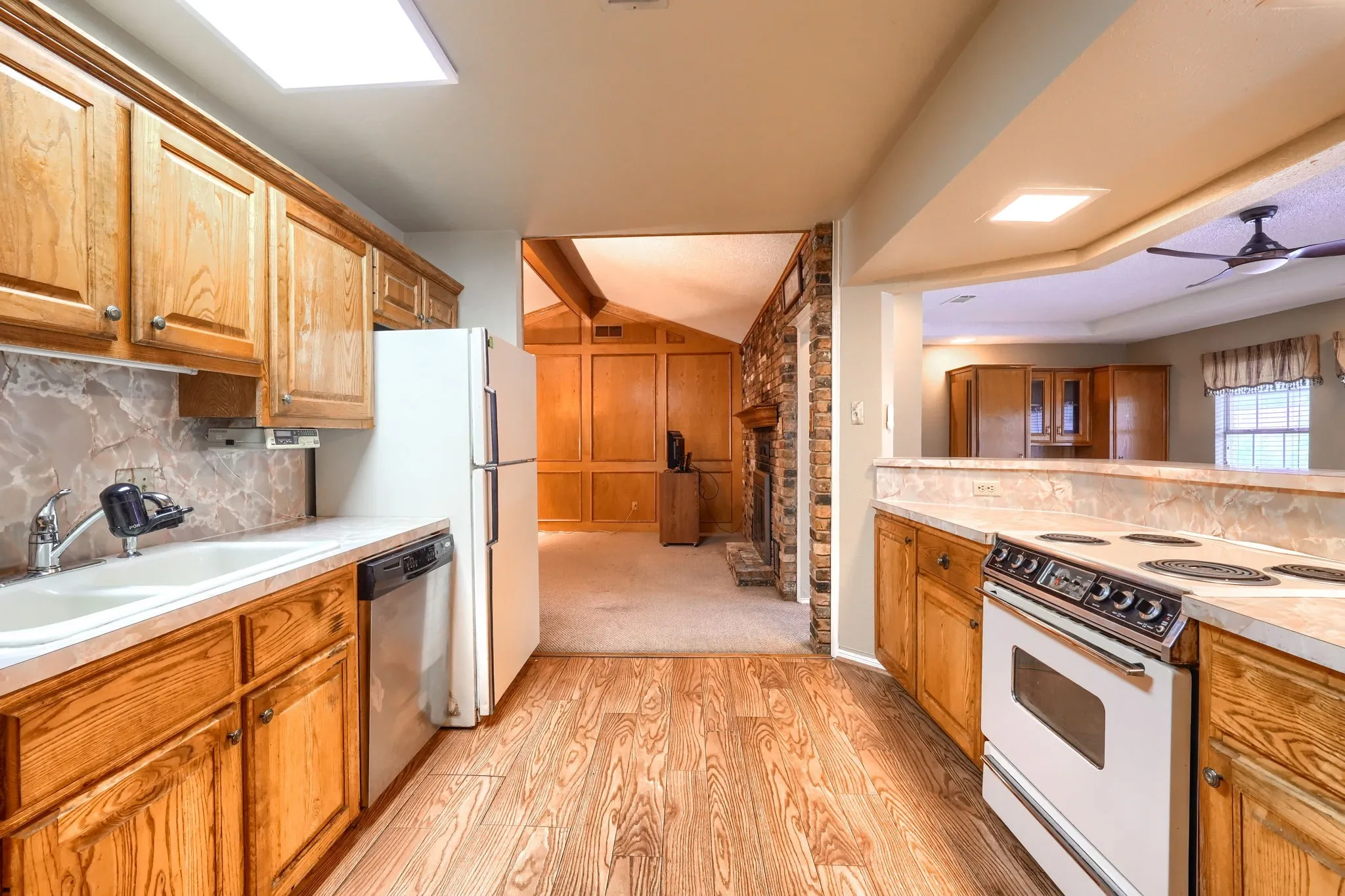 Kitchen with wood-finish flooring, oak cabinetry, and stone-look backsplash