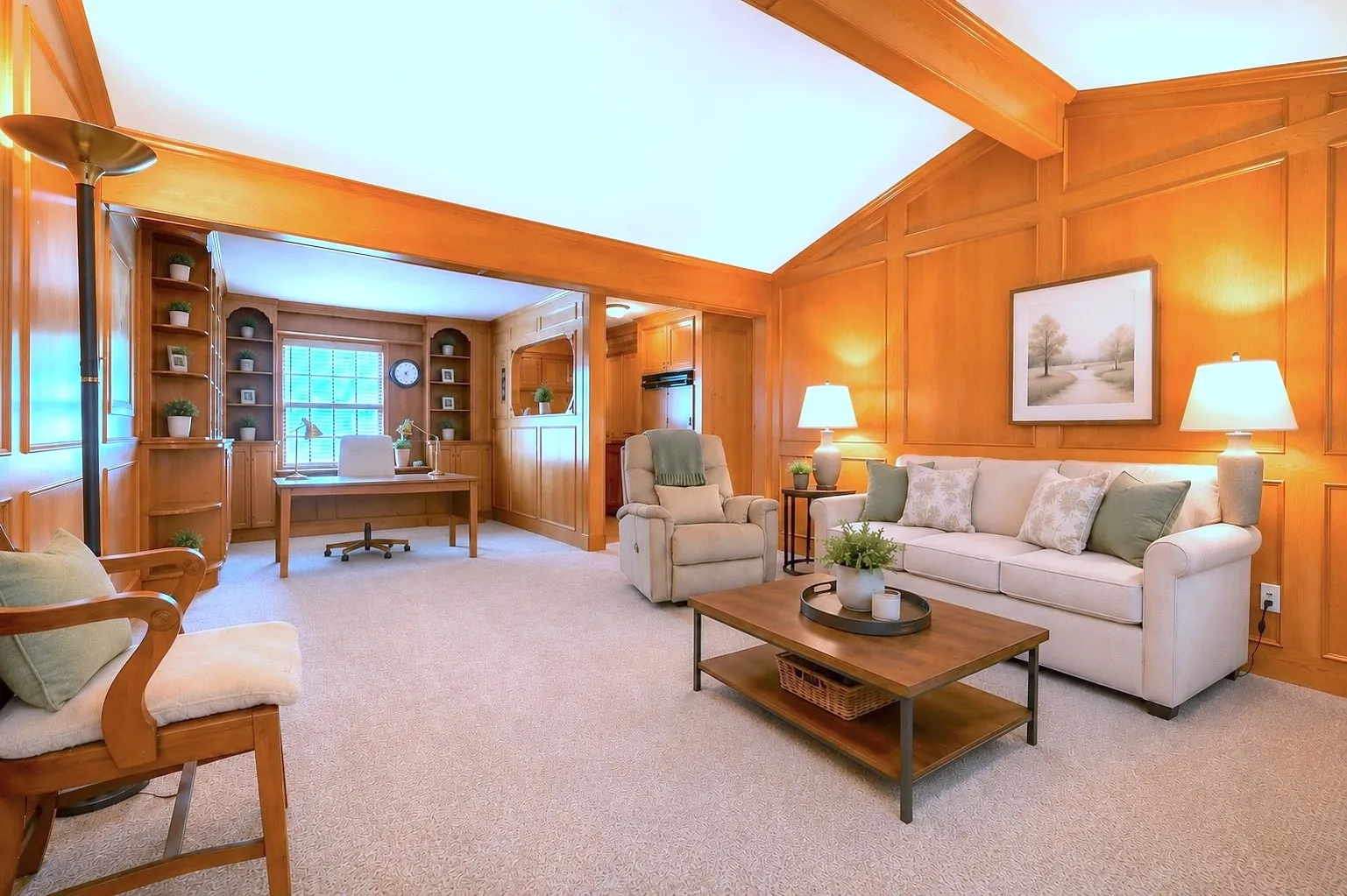 Paneled living space featuring a vaulted ceiling with exposed beam, wall-to-wall carpeting, and an integrated office area with built-in shelving- AI