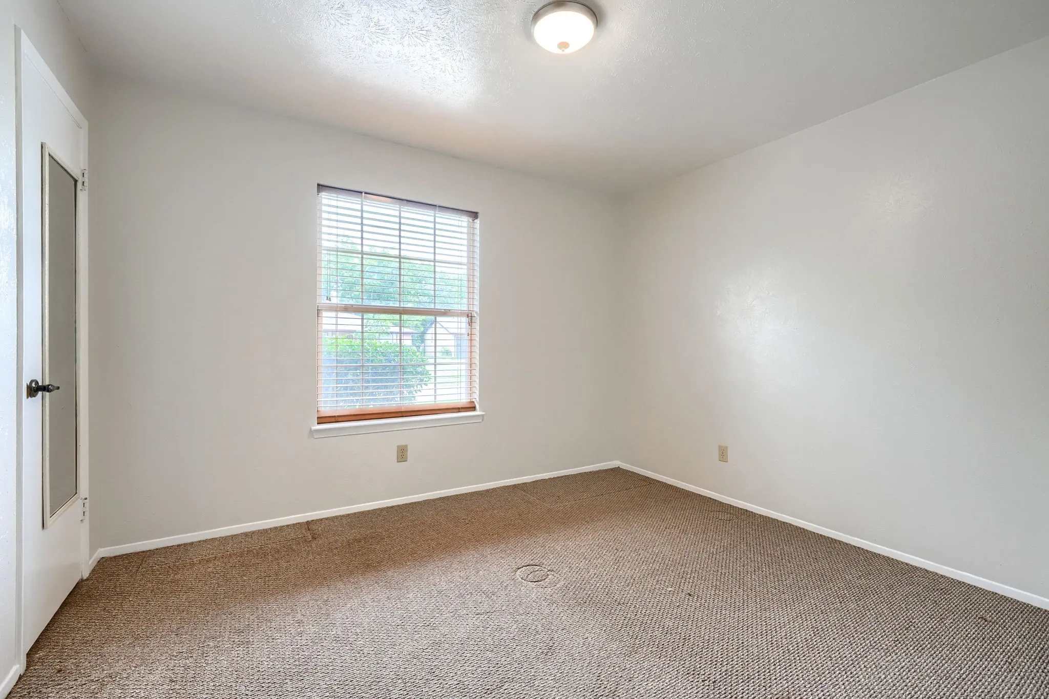 Carpeted room with a window featuring horizontal blinds and a wood-finish sill