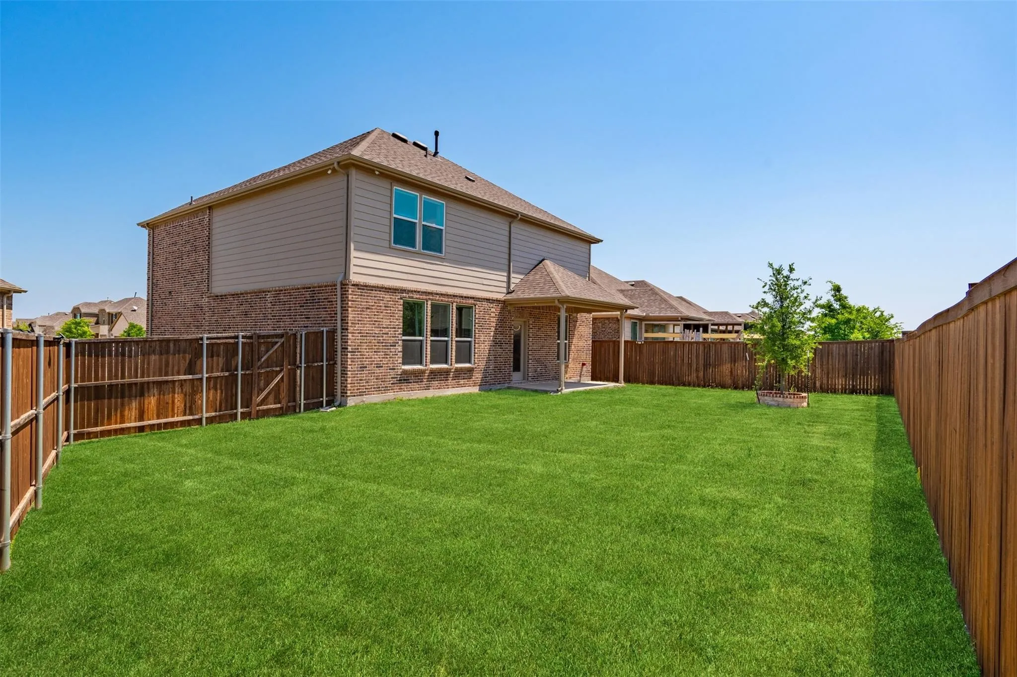 Spacious backyard featuring a manicured lawn, full privacy fencing, and a covered patio area