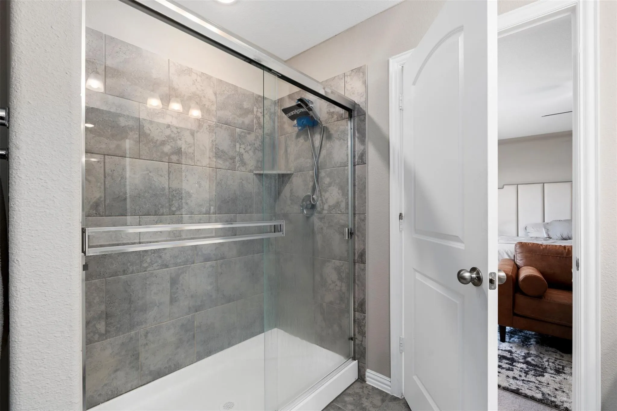 Glass-enclosed shower featuring large format gray tile, a built-in shower niche, and a rain showerhead