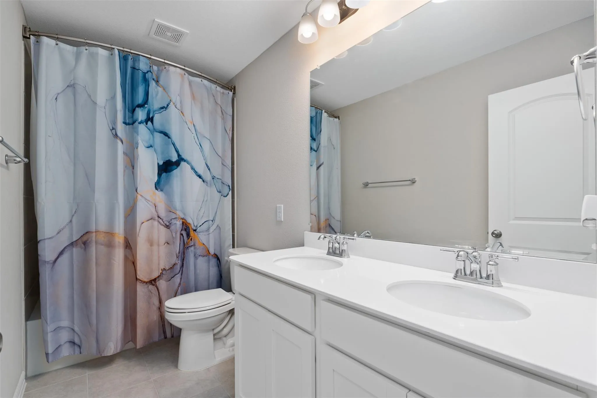 Bathroom featuring a dual-sink vanity with white cabinetry, a large wall-mounted mirror, overhead vanity lighting, and a combination tub and shower
