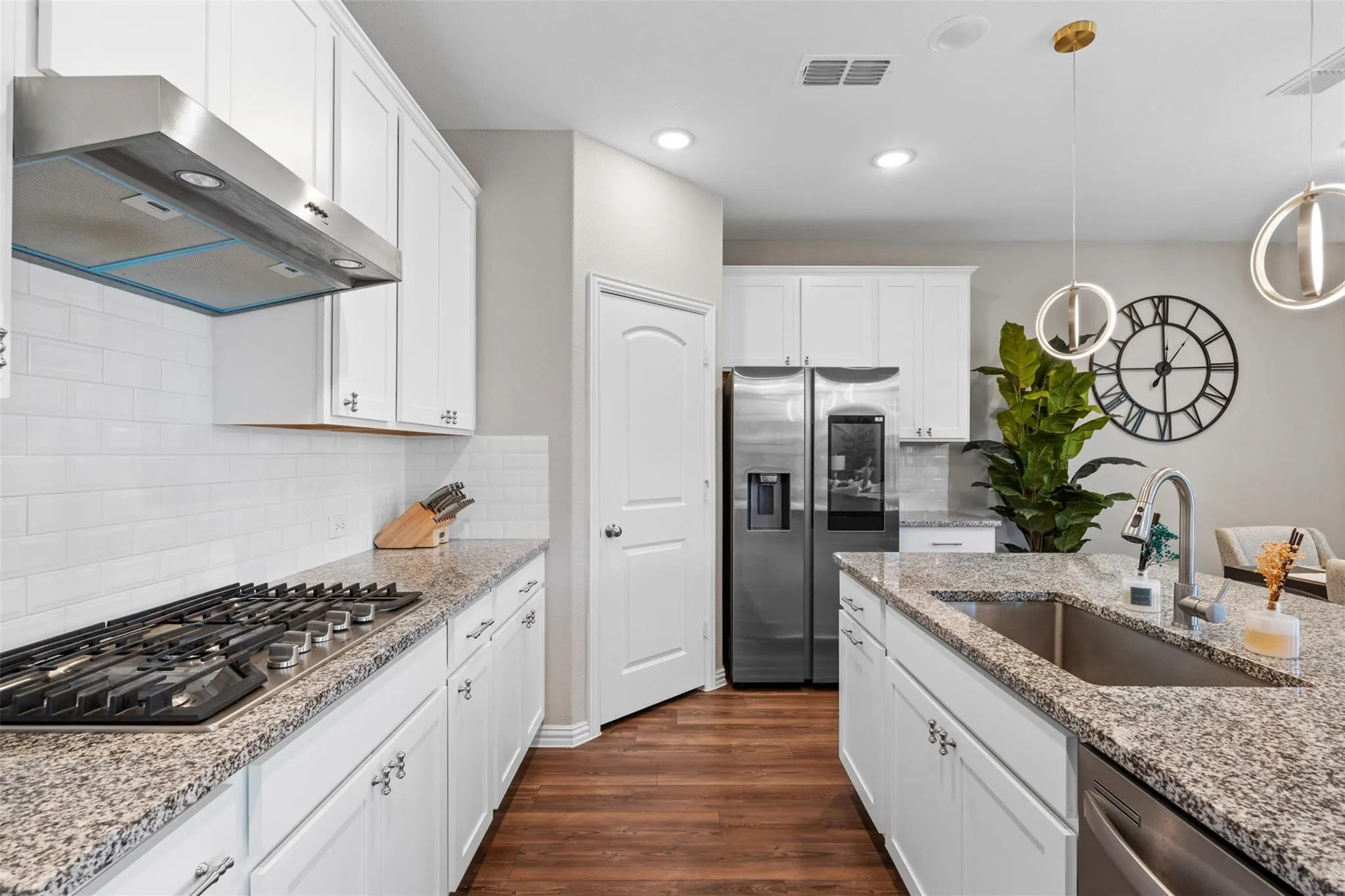 Modern kitchen featuring white cabinetry, granite countertops, wood-finish flooring, a stainless steel range hood, and a built-in stainless steel sink