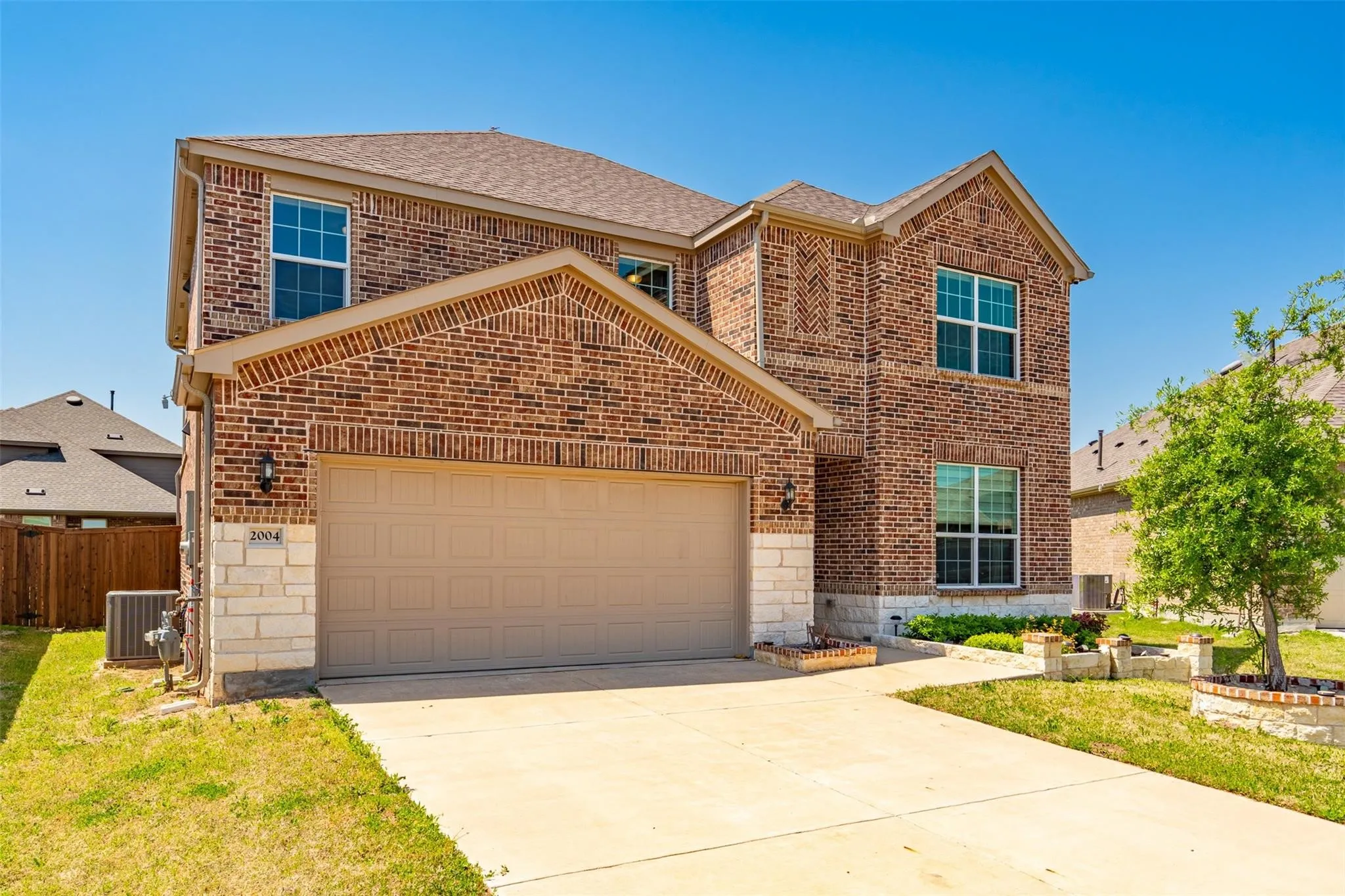 Two-story brick and stone facade residence featuring a two-car garage, multiple grid-pane windows, and a concrete driveway
