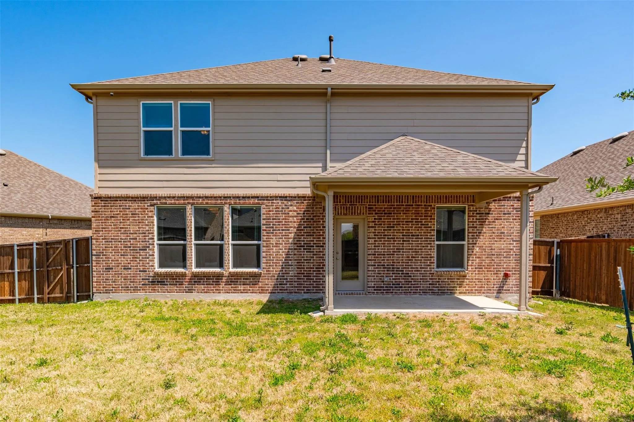 Two-story exterior with brick and siding facade, featuring a covered patio with concrete flooring, multiple windows, and a shingle roof