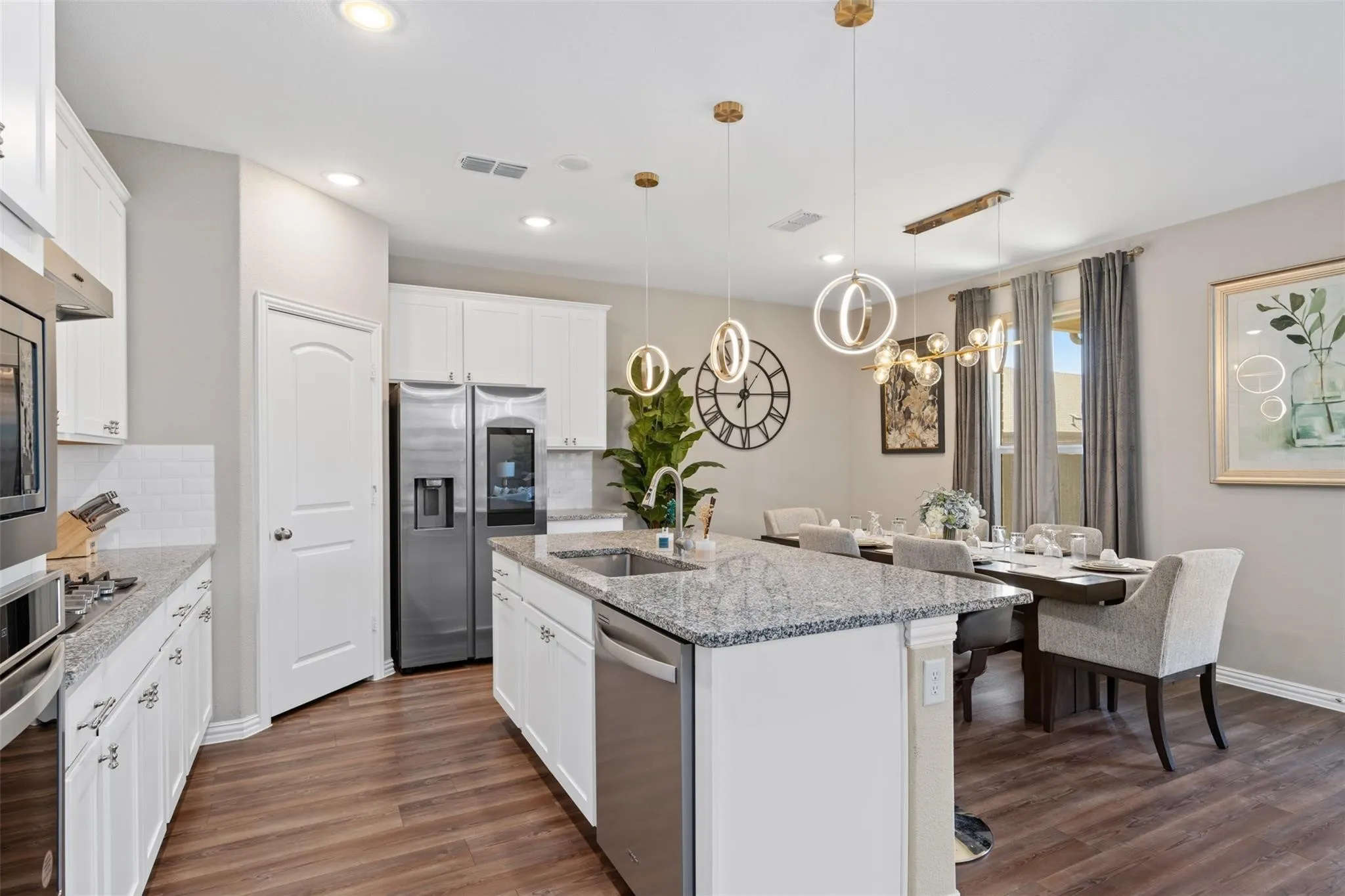 Modern kitchen featuring a central island with an integrated sink, stainless steel appliances, white cabinetry, and wood-finish flooring