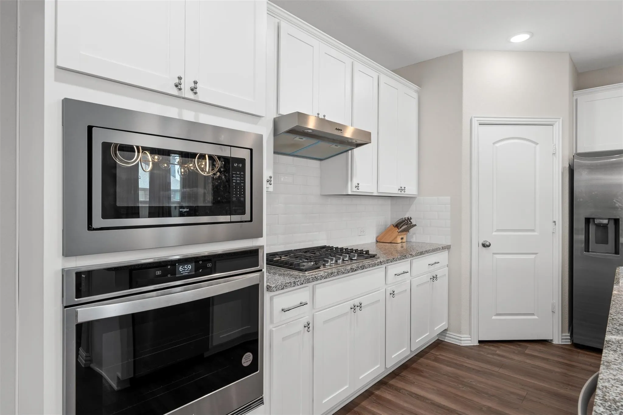 Modern kitchen featuring white cabinetry, stainless steel appliances, a subway tile backsplash, granite-finish countertops, and wood-finish flooring