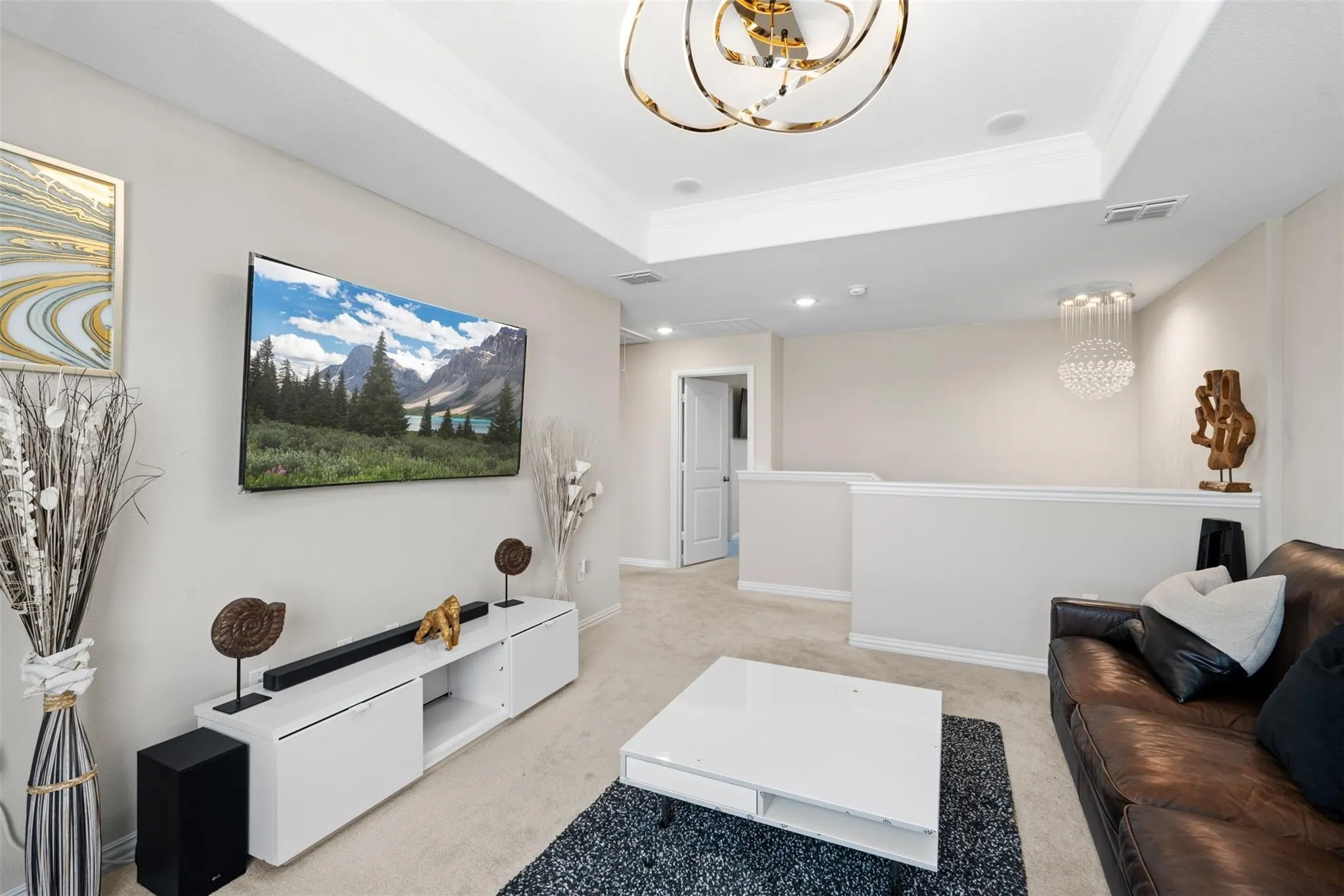Carpeted loft area featuring a tray ceiling with a contemporary chandelier, a built-in entertainment console, recessed lighting, and a white half-wall railing