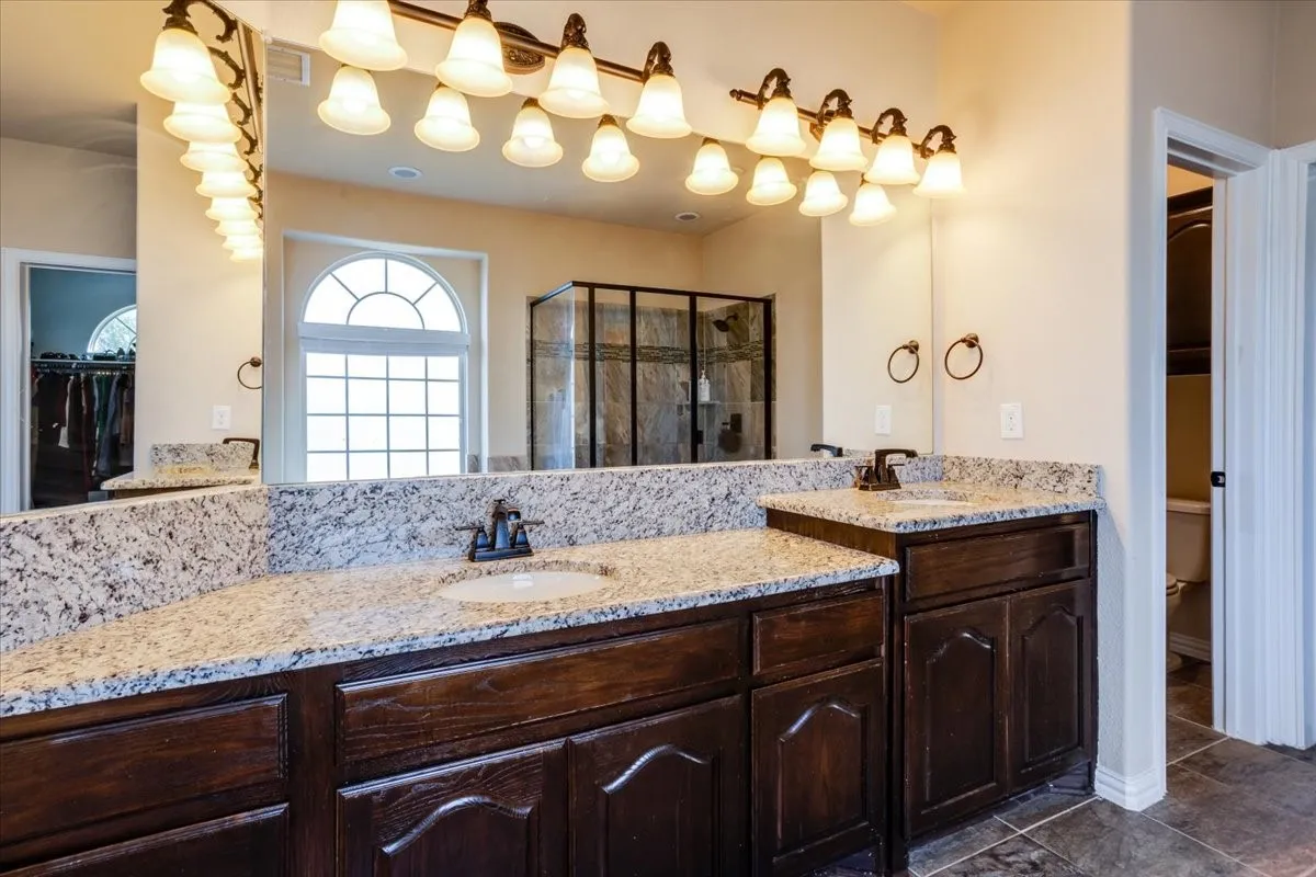 Bathroom featuring double vanity, a shower stall, a spacious closet, and dark tile patterned floors