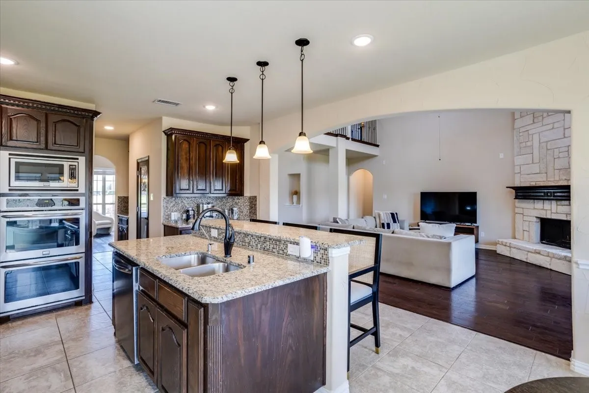 Kitchen featuring arched walkways, light tile patterned floors, dark wood finish cabinets, and light stone counters