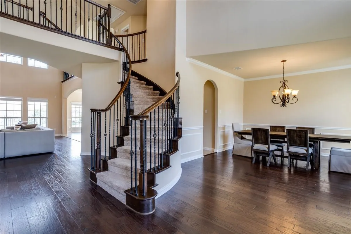 Entryway featuring arched walkways, dark wood-type flooring, crown molding, hanging lights, and a high ceiling