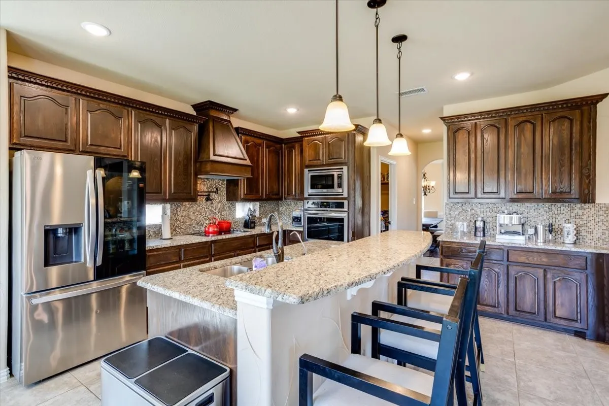 Kitchen with stainless steel appliances, arched walkways, light tile patterned floors, hanging light fixtures, and light stone counters