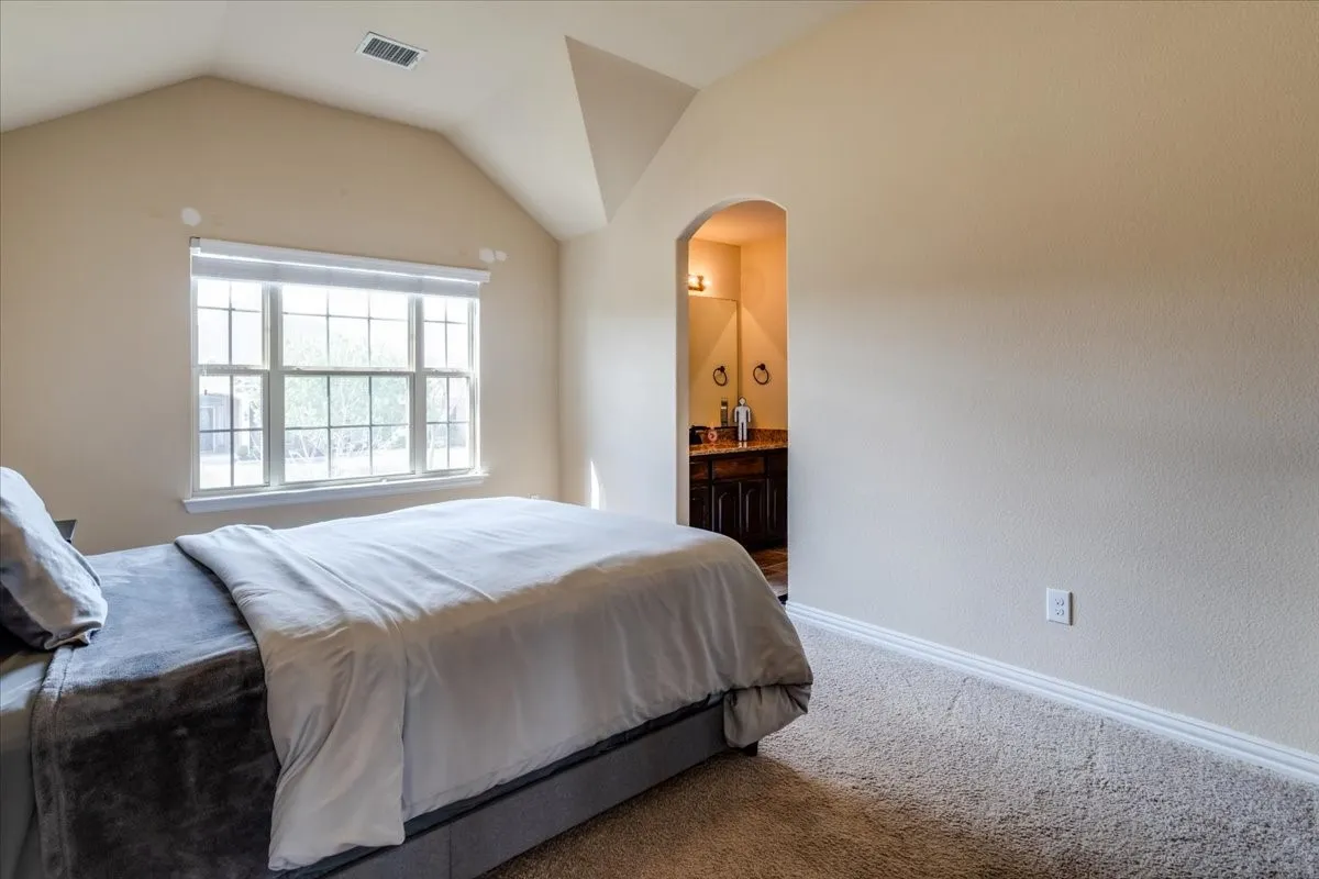 Carpeted bedroom featuring arched walkways, ensuite bathroom, and lofted ceiling