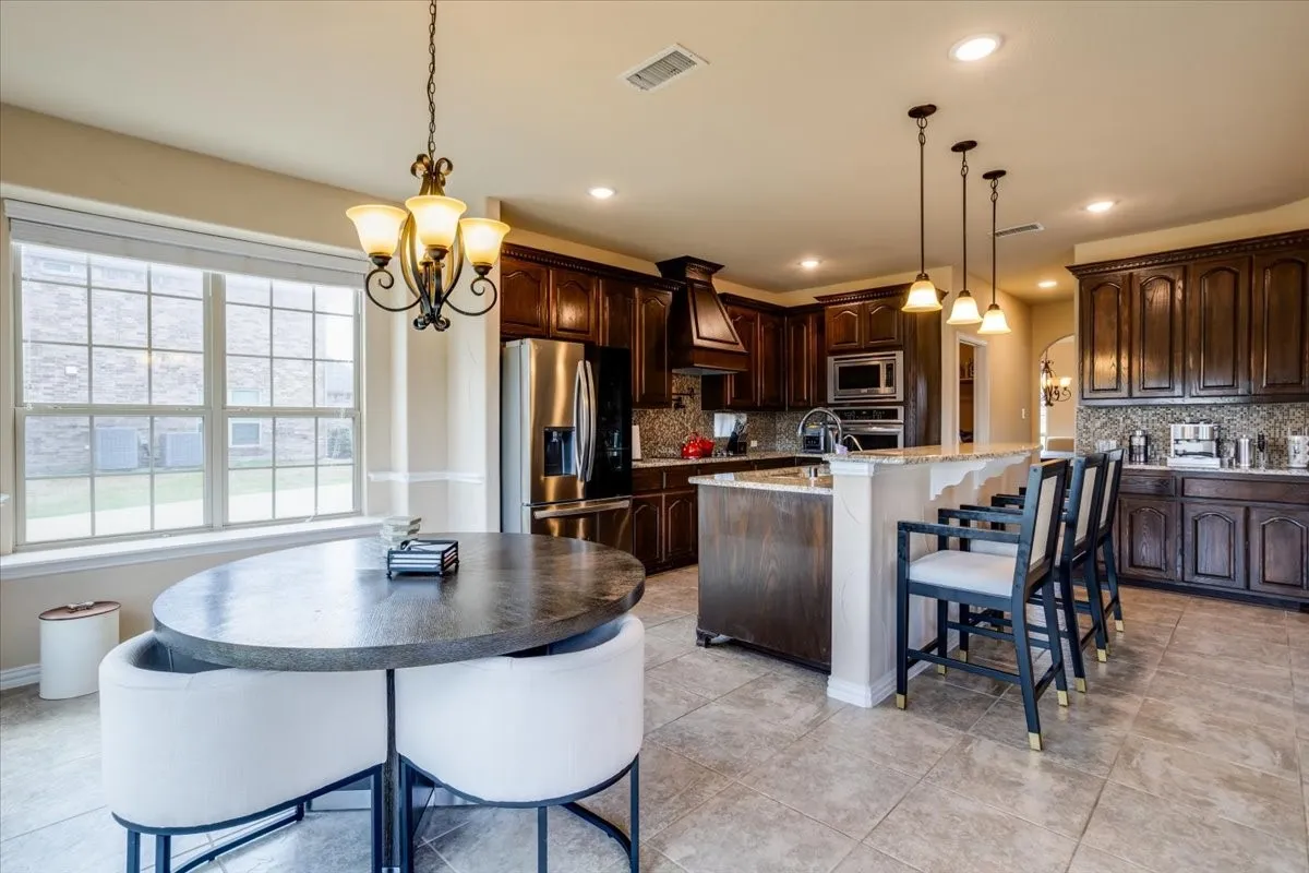 Kitchen featuring dark wood finish cabinets, stainless steel appliances, arched walkways, light stone counters, and a kitchen island with sink